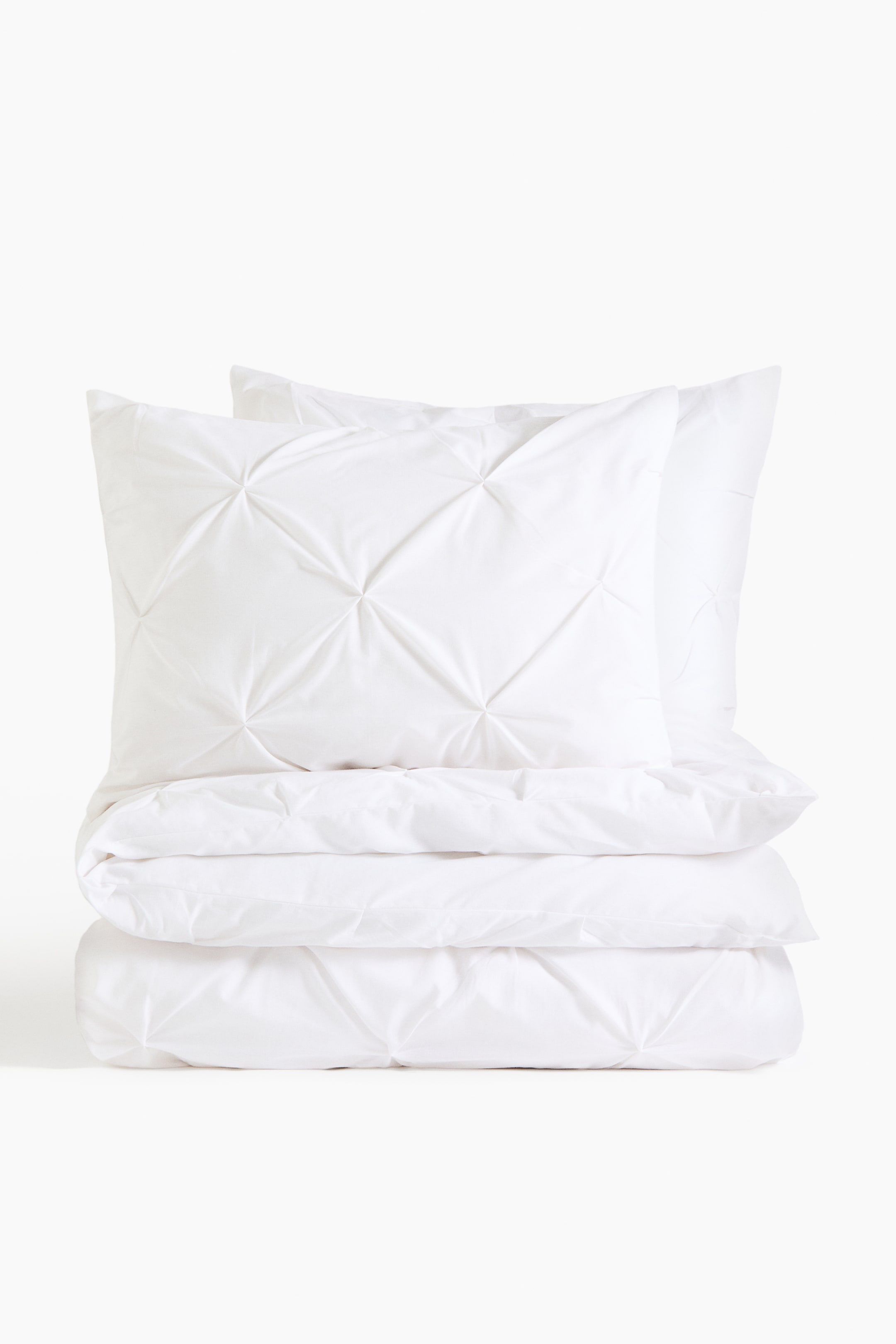 View larger image: A white bedding set showcases two pillows stacked atop a folded white duvet. The FRONT pillow exhibits a diamond-patterned pintuck design, which is also evident on the folded duvet.
