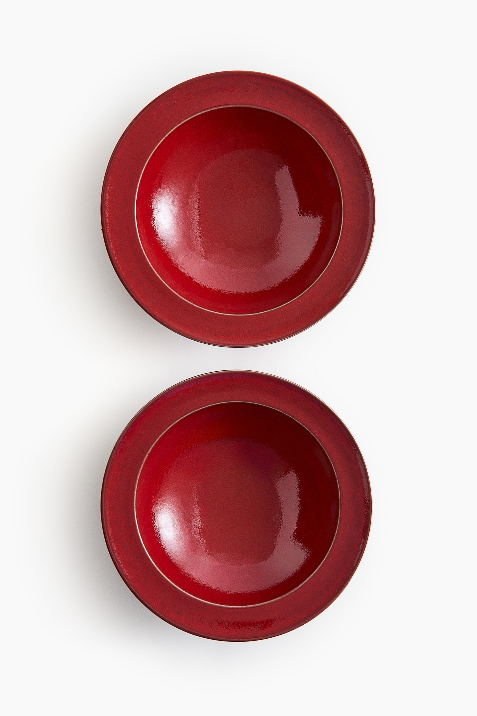 Δύο βαθιά πιάτα από stoneware παρουσιάζονται από επάνω, αναδεικνύοντας ένα πλούσιο κόκκινο reactive glaze με γυαλιστερό φινίρισμα. Τα πιάτα διαθέτουν ένα κλασικό φαρδύ χείλος που περιβάλλει ένα βαθύ κυκλικό κέντρο. - 1