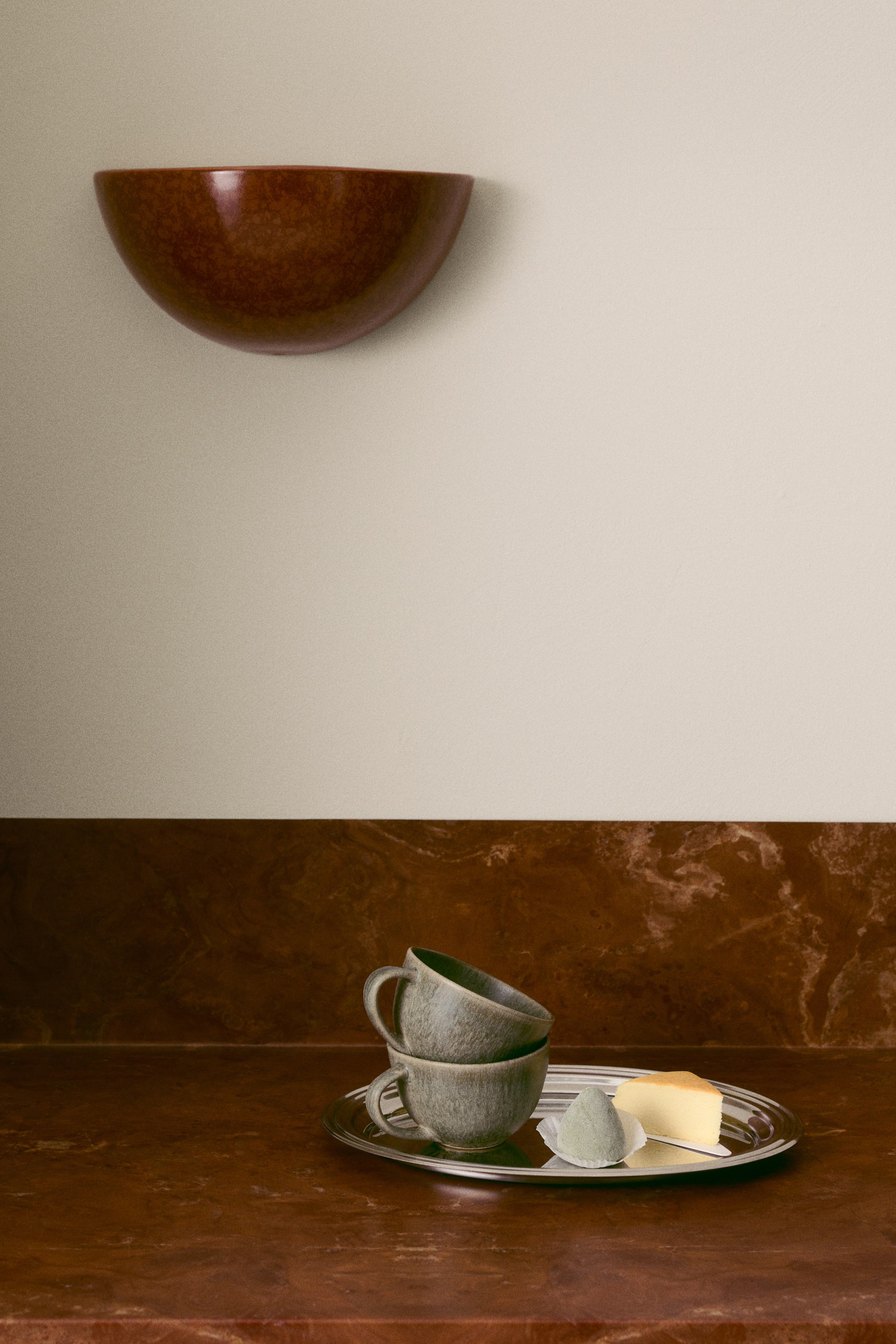 View larger image: Two stoneware tea mugs featuring a mottled grey-green reactive glaze are resting stacked on a silver tray, with the top mug tilting slightly inside the bottom one. Each mug is designed with a rounded body and a small curved handle on the side.