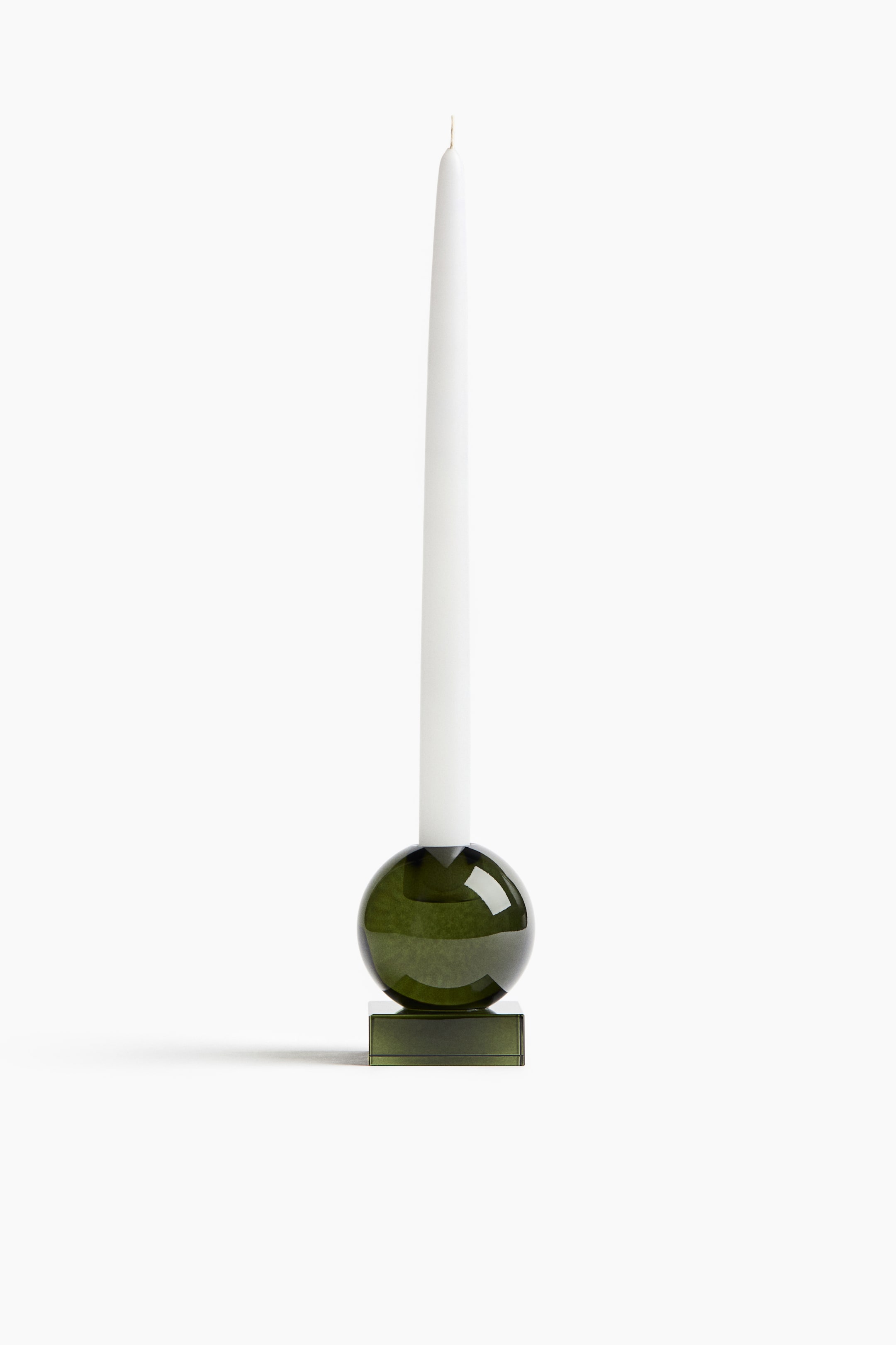 View larger image: A translucent olive-green glass candle holder is holding a tall, white taper candle, viewed from the front. The candle holder features a spherical upper body resting on a flat, square base.