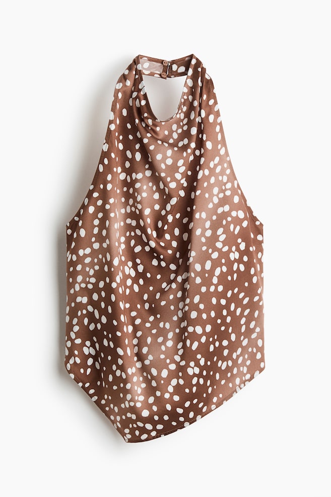 A brown halter top featuring a white spotted pattern is displayed from a front-facing angle, showcasing a draped cowl neckline and a high collar band with button closures. The top is made of a smooth, satin-like fabric and features an asymmetrical hemline. - 1