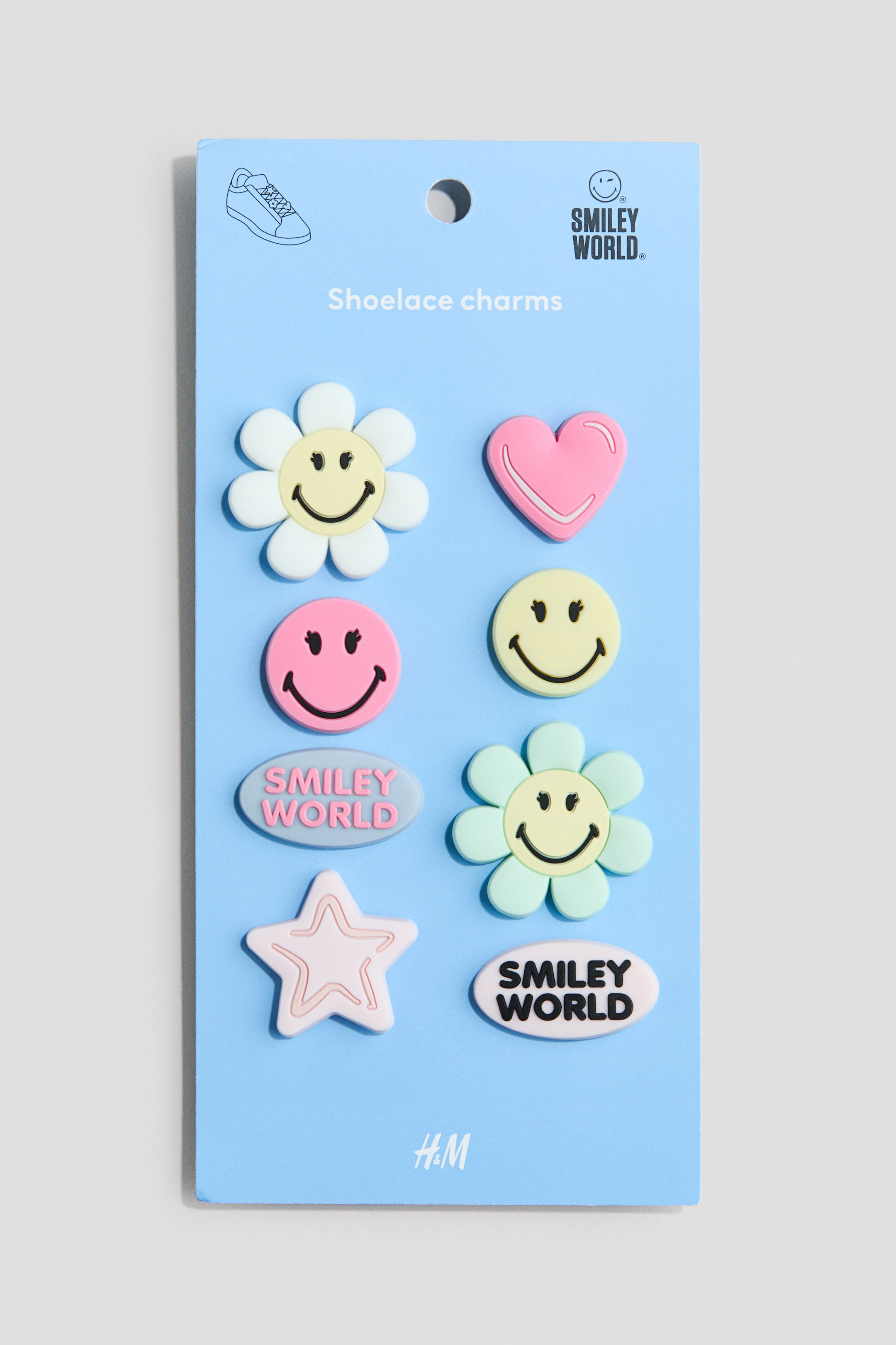 View larger image: Shoelace charms are presented on a light blue rectangular card, showcasing eight assorted designs. The charms include white and light green flowers with yellow smiley faces, pink and yellow circular smiley faces, a pink heart with a white outline, a pink star with a white outline, a light grey oval with pink "Smiley World" text, and a white oval with black "Smiley World" text.