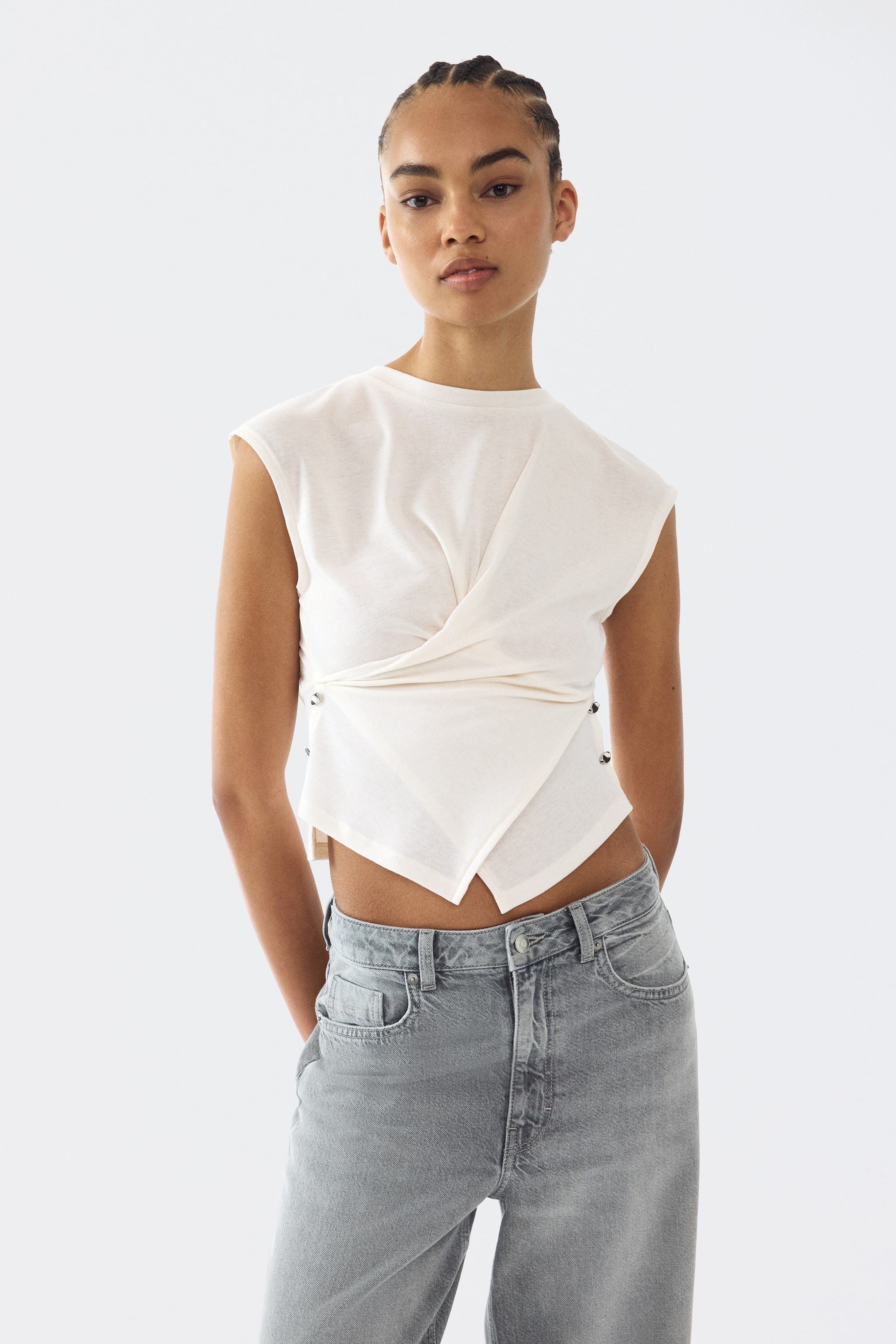 View larger image: The cream top boasts a crew neck and cap sleeves, with its wrap-front design forming a V-shaped cropped hem that fastens on both sides with visible metal snaps.