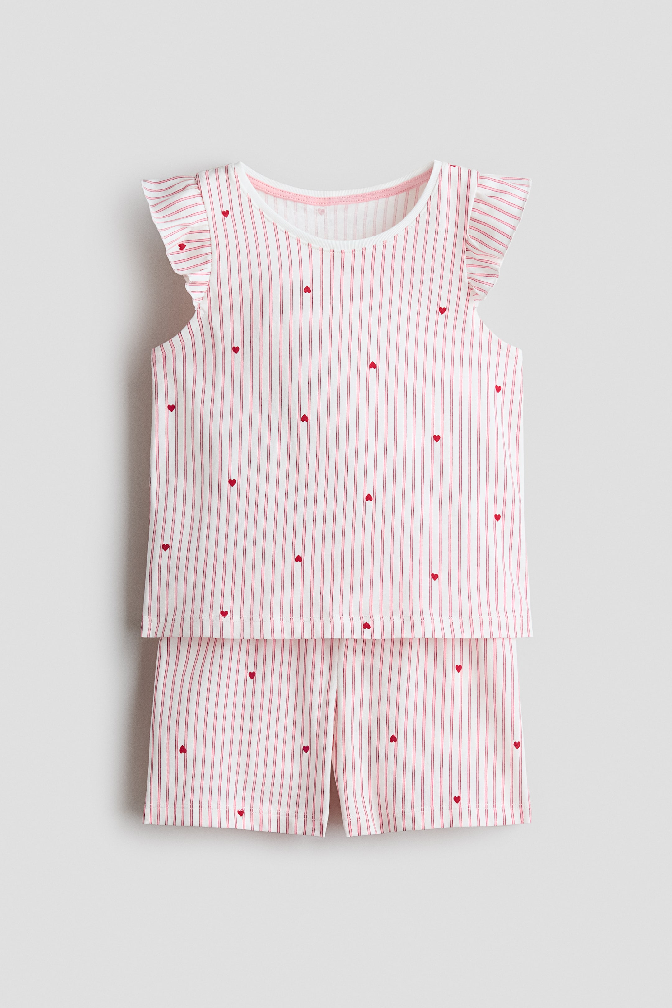 View larger image: A pajama set is showcased with a front-facing view, comprising a sleeveless top and matching shorts. The top displays ruffled cap sleeves and a ribbed crew neck. Both pieces are adorned with thin red vertical stripes and scattered small red hearts on a white background.