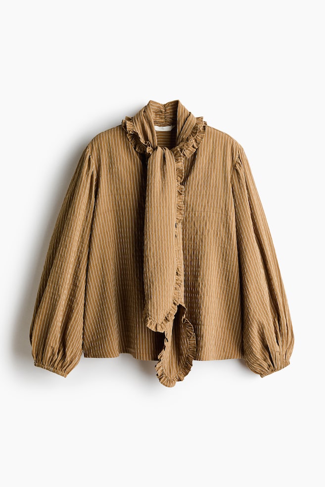 A brown and white striped blouse in a textured weave is shown from the front, featuring a ruffled scarf collar tied loosely at the neck. The blouse features long balloon sleeves with elasticated cuffs and a relaxed, loose-fitting silhouette. - 1