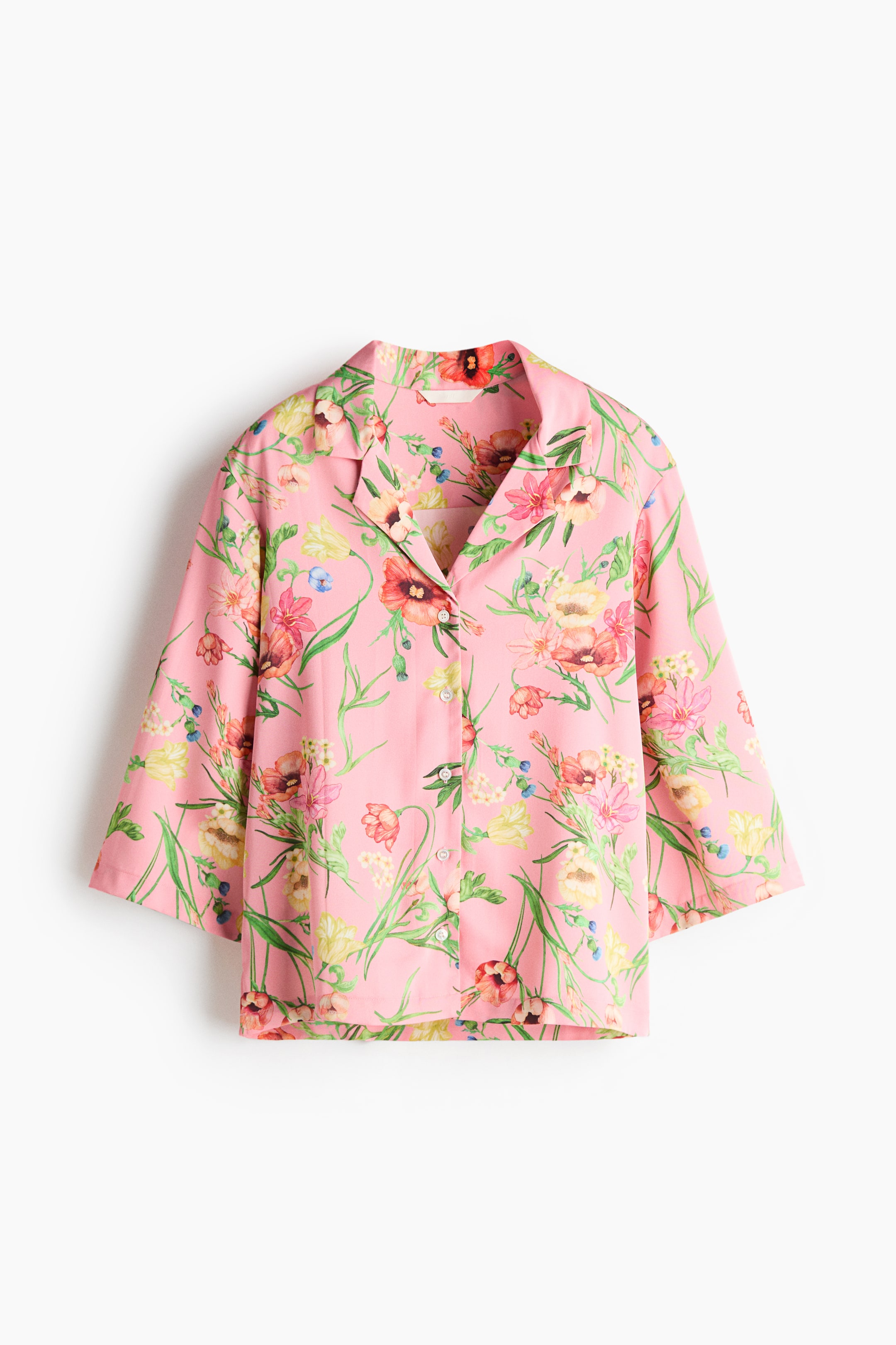 View larger image: A front-facing pink shirt features a multicolored floral pattern. It has an open camp collar, three-quarter-length sleeves, and light-colored buttons down the front.