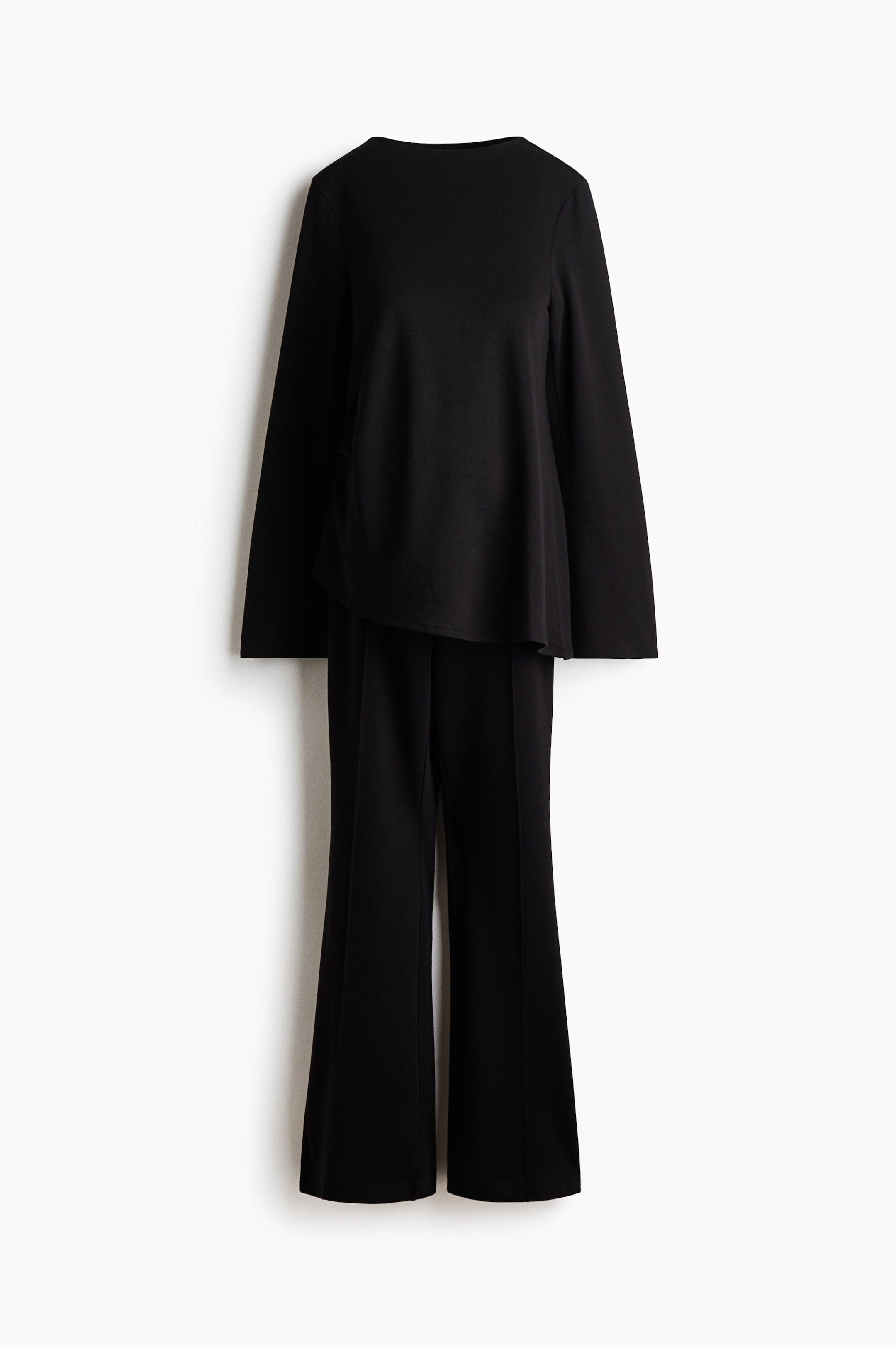 View larger image: A black two-piece set featuring a boat-neck top with wide long sleeves and an asymmetrical hem, layered over wide-leg trousers with a pressed front crease.