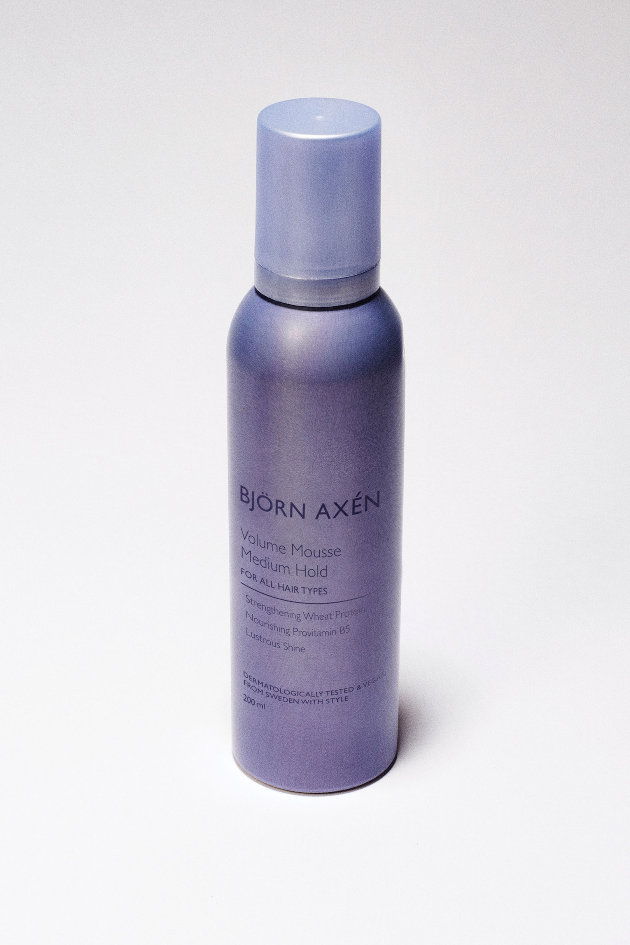 Visualizza immagine più grande: Un flacone di Björn Axén Volume Mousse è in posizione verticale, leggermente inclinato verso l'osservatore. Il flacone cilindrico è di un viola metallico con un tappo di un viola più chiaro, e il testo bianco identifica il prodotto come 'Volume Mousse Medium Hold' insieme ad altri dettagli.