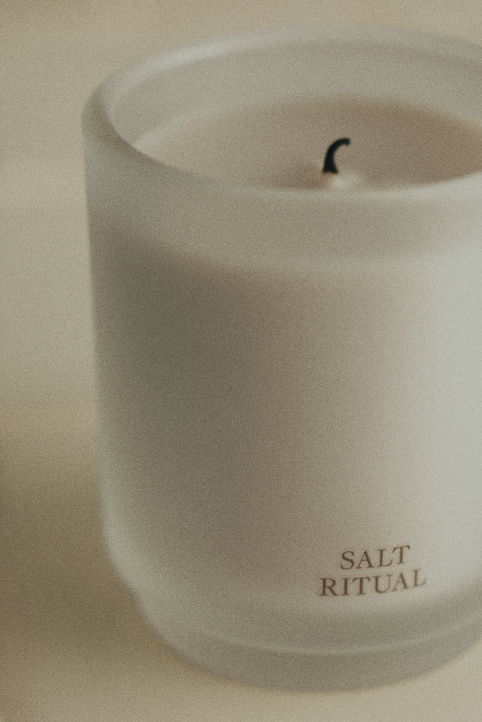 A cylindrical scented candle in a frosted glass container contains white wax and displays 'SALT RITUAL' on its lower front. It is presented alongside its rectangular white packaging box, which features 'SALT RITUAL' vertically, 'SCENTED CANDLE 255 g 8.99 oz.', and a list of scent notes: eucalyptus, apple, lily of the valley, salt accord, cedarwood, and musk. - 1
