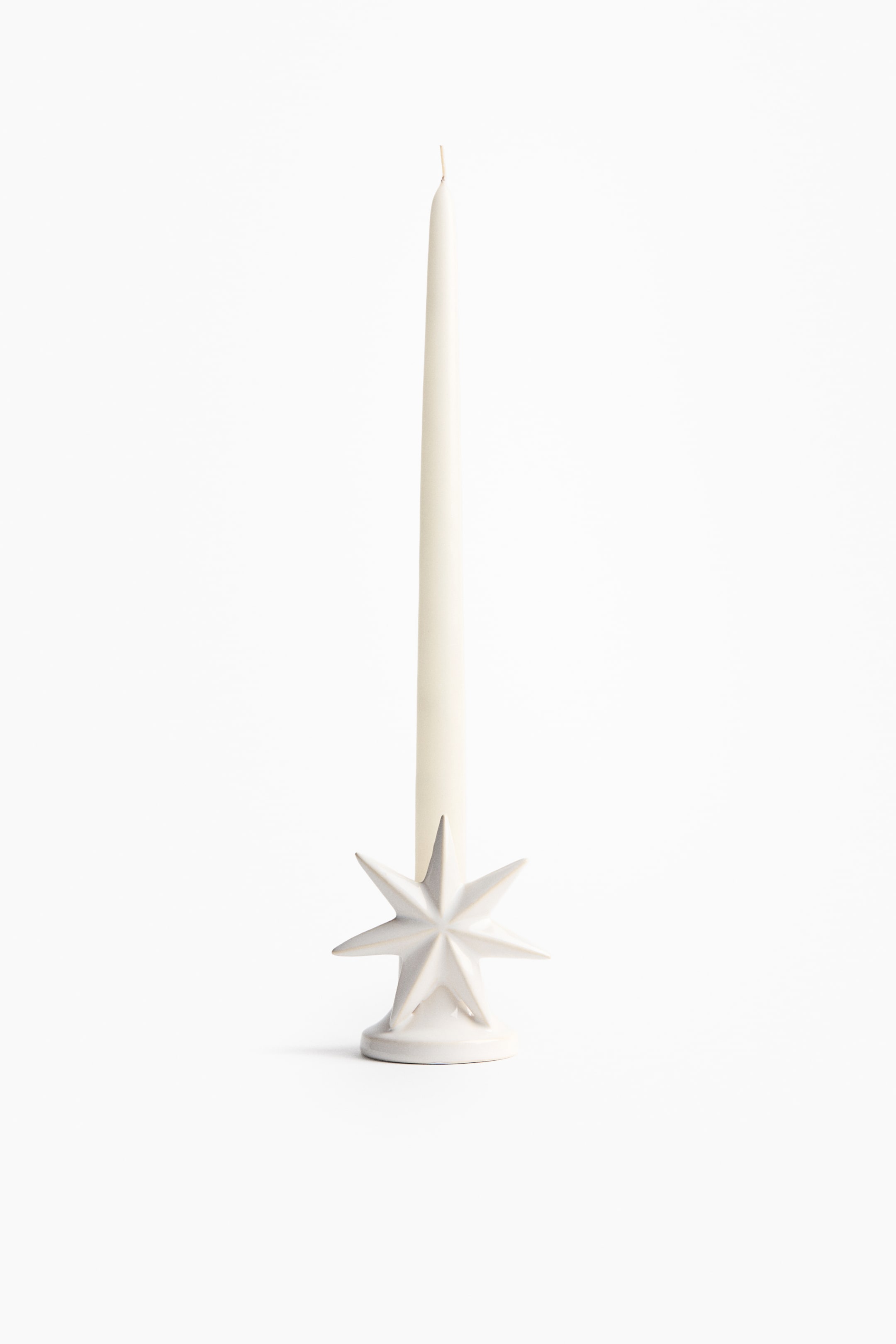 View larger image: A light-colored stoneware candlestick features a multi-pointed star design on a rounded base, holding a slender, light-colored taper candle upright.