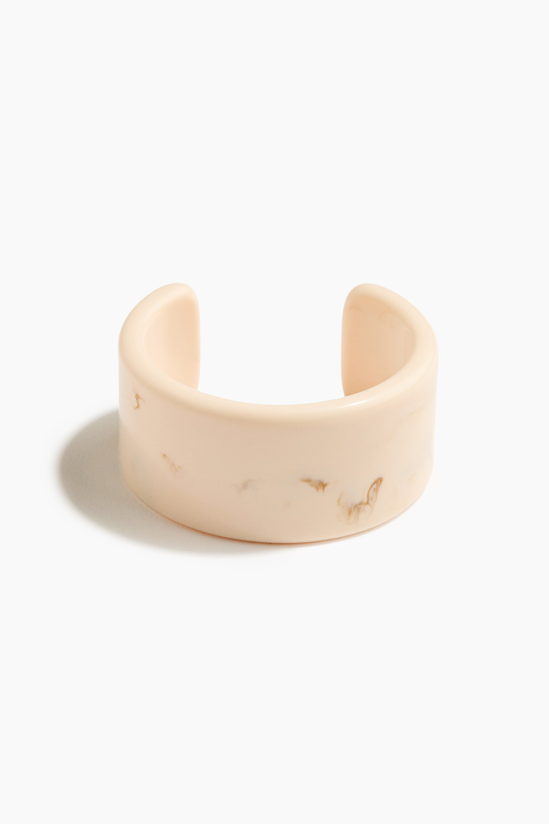 View larger image: A wide, pale-peach cuff bracelet is shown from the front, featuring an open design with rounded edges and a smooth, glossy surface with subtle brown marbling.