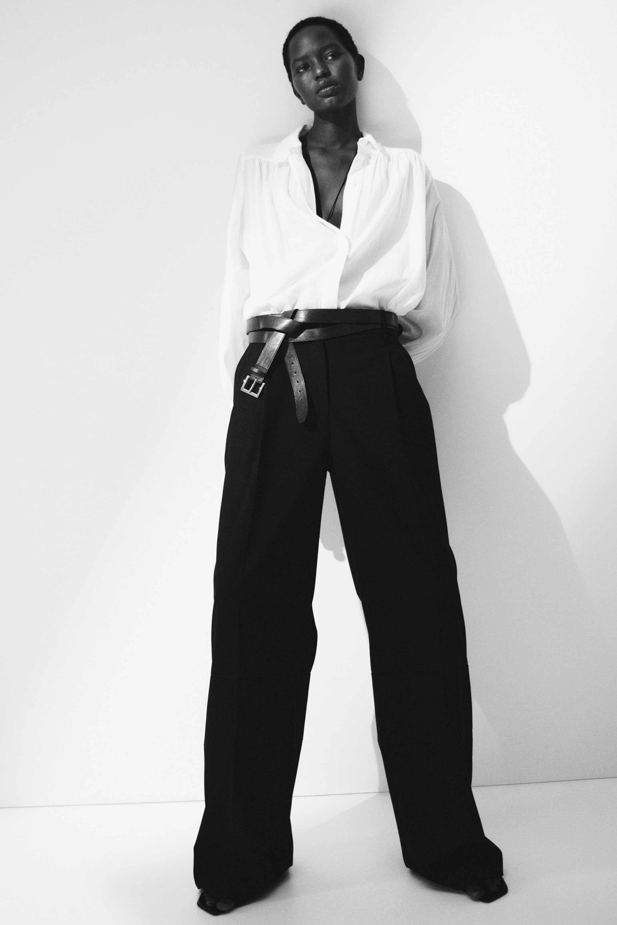 View larger image: A white relaxed-fit shirt with an open collar is being tucked into black wide-leg pleated pants. A black leather belt is wrapping multiple times around the waist, cinching the shirt and pants.