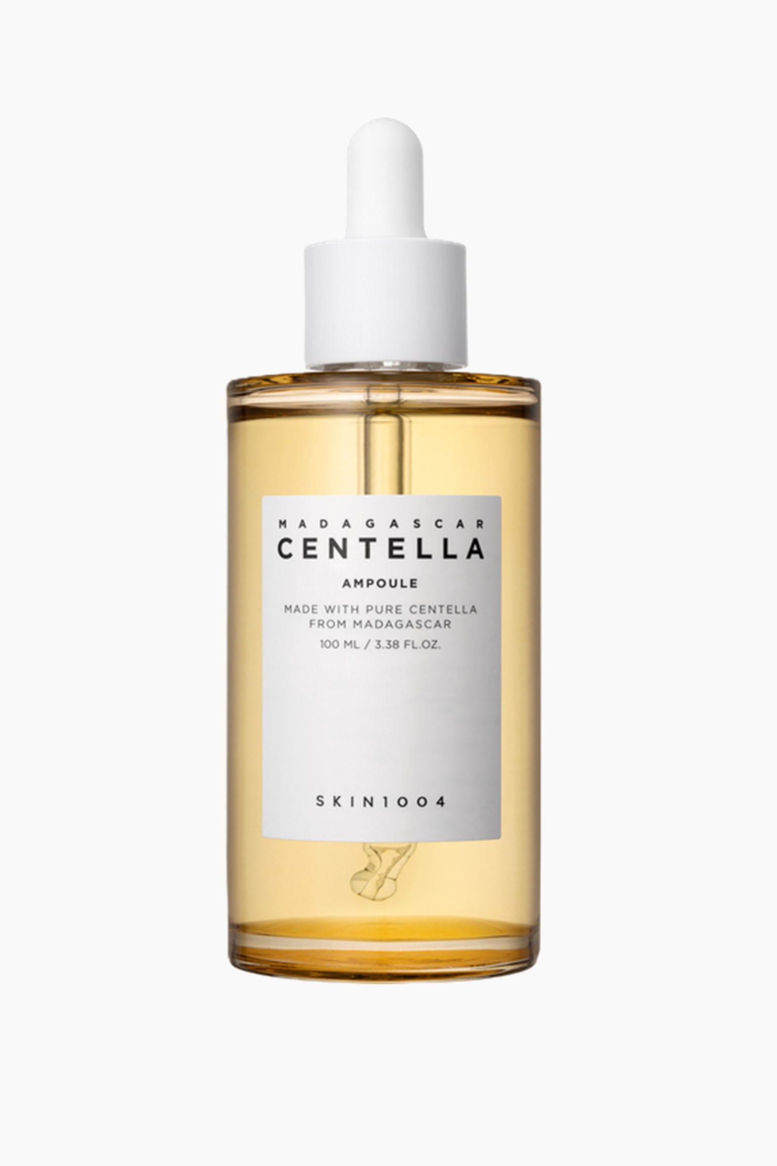 En klar, rektangulær glassflaske som inneholder en gul væske står oppreist, med en hvit pipettekork og en gjennomsiktig glasspipette inni. En hvit etikett på forsiden viser "MADAGASCAR CENTELLA AMPOULE" og "SKIN1004." - 1