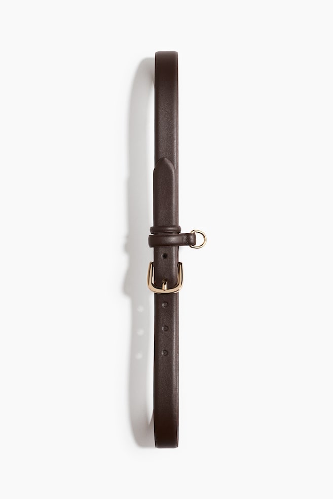 A narrow, dark brown belt is lying flat, featuring a gold-toned rectangular buckle with a single prong. A matching dark brown keeper with a small gold-toned D-ring is also visible near the buckle. - 1