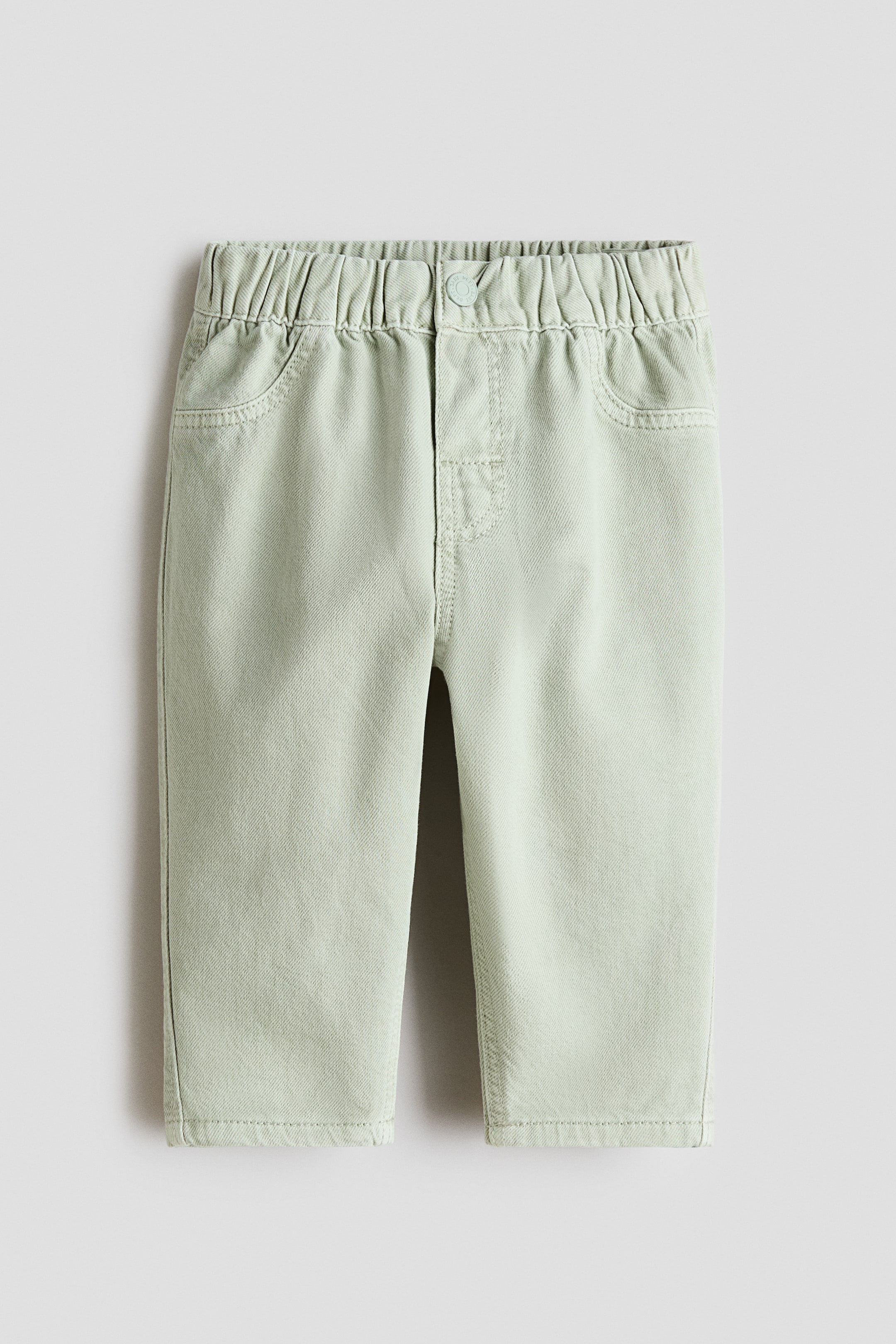 View larger image: Trousers in a light green, soft cotton weave are presented from the FRONT, featuring an adjustable, elasticated waist, a fake fly with a press-stud, and decorative front pockets.