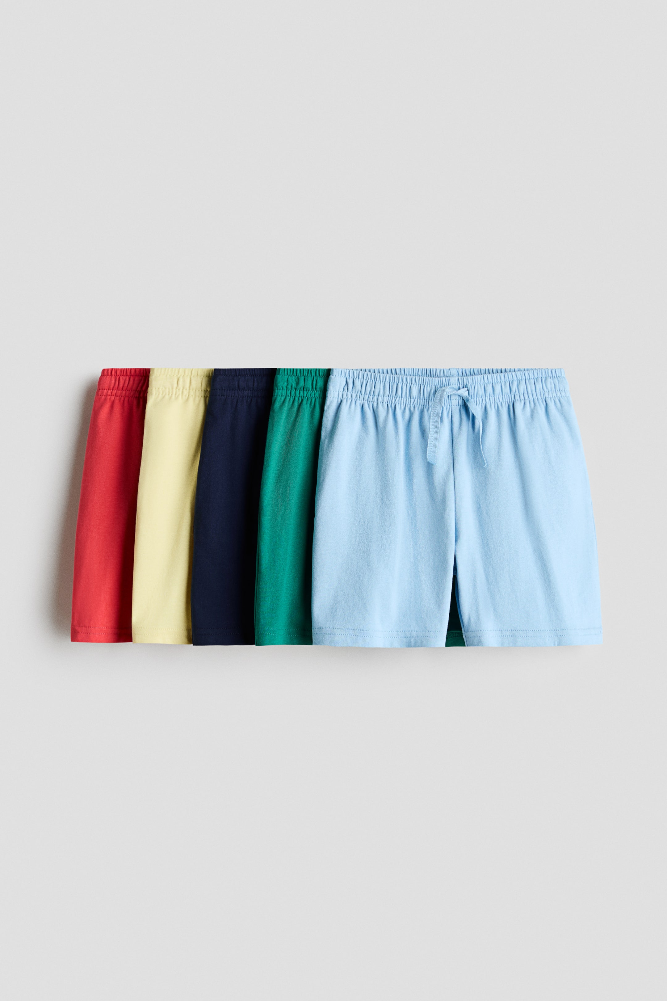 Voir une image plus grande: Cinq paires de shorts en jersey de coton doux sont disposées en ligne horizontale, chacune présentant une taille élastiquée. Les shorts apparaissent en rouge, jaune, bleu marine, vert et bleu clair, avec la paire avant en bleu clair affichant un cordon de serrage visible.