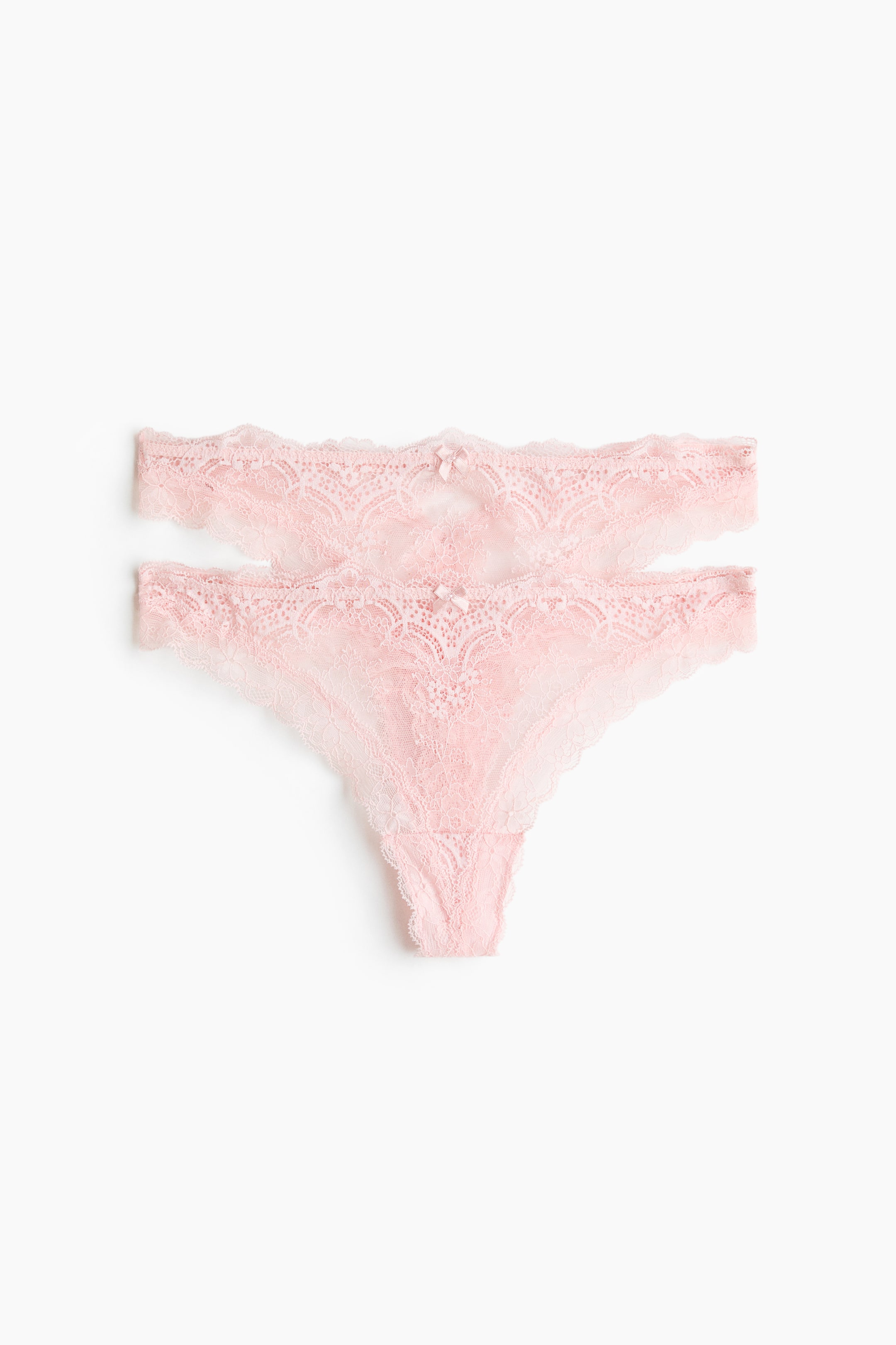 Größeres Bild ansehen: Zwei rosa Spitzen-Stringtangas präsentieren ihre Vorderansicht, jeweils mit mittlerer Taille, zarten Blumenmustern, einer kleinen Schleife vorne in der Mitte und einem gefütterten Zwickel.