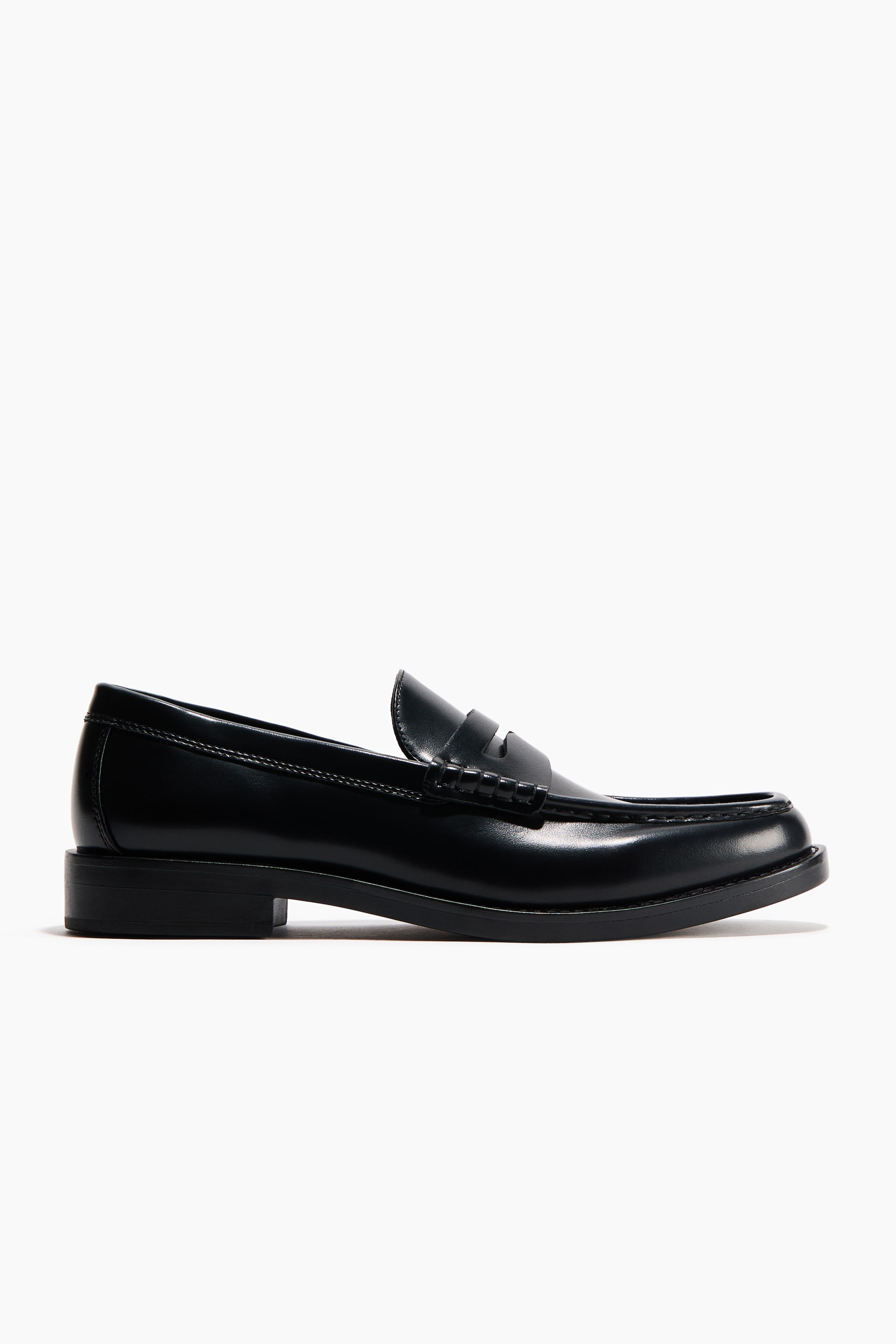 View larger image: A black polished leather loafer is showcasing an apron toe and a penny strap across the vamp, with a low block heel and a visible stacked sole, presented from a side profile.