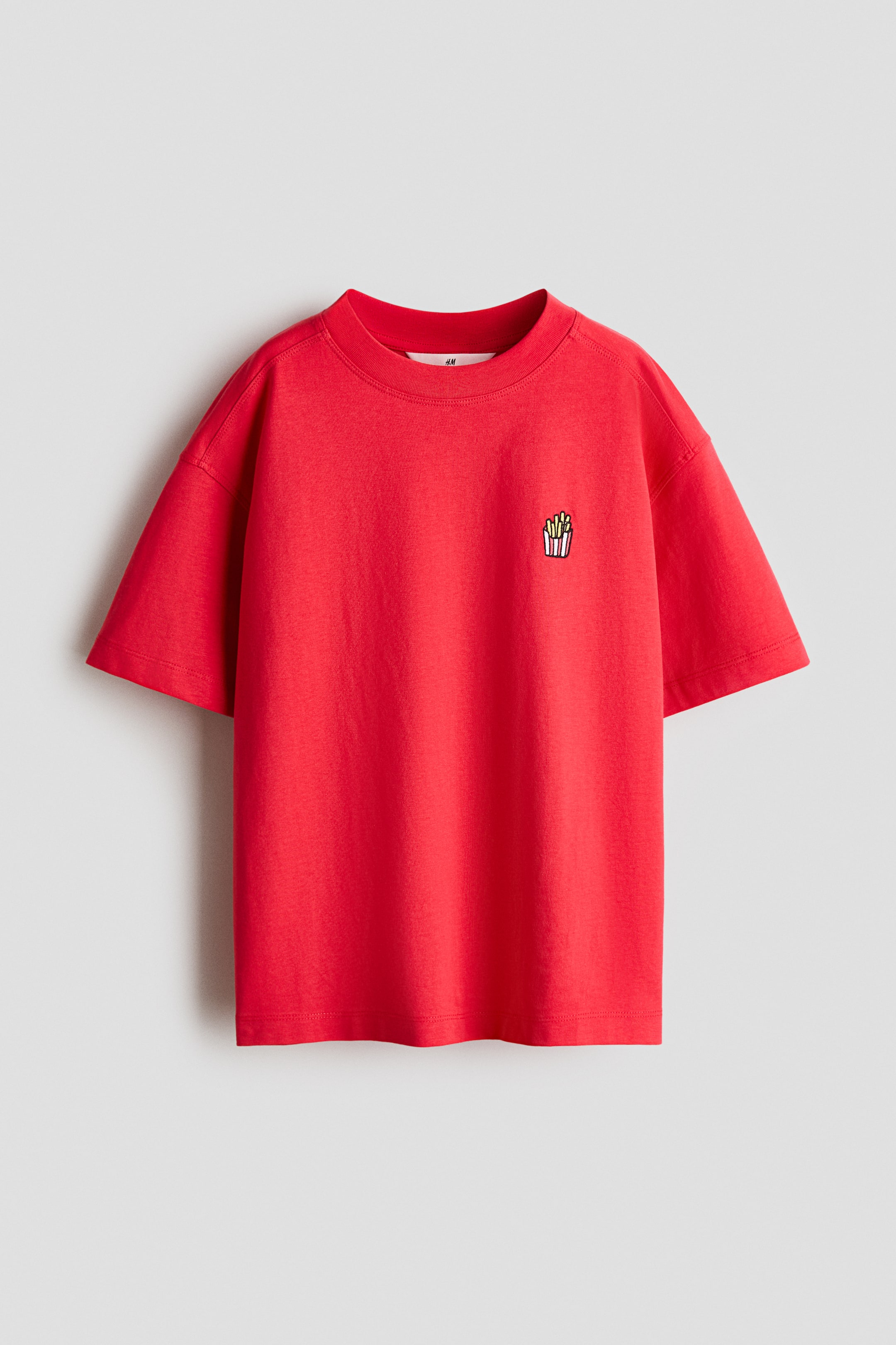 拡大画像を表示: 赤いクルーネックのTシャツが前面を見せており、短い袖と左胸に刺繍されたフレンチフライのグラフィックが特徴です。