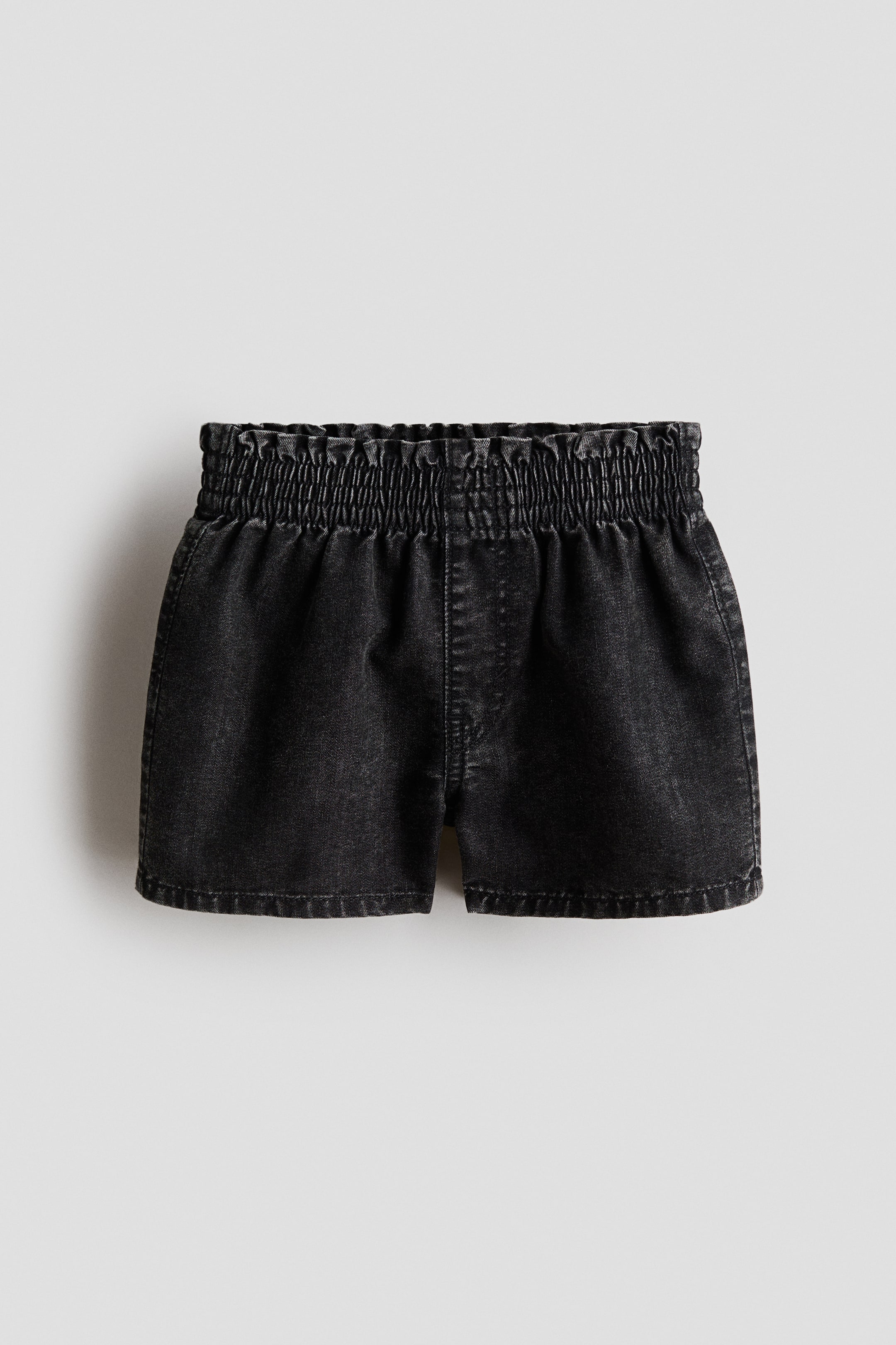 View larger image: The front of these loose-fit shorts showcases a washed black lightweight denim, a smocked elasticated pull-on waist, a faux fly detail, and visible side pockets.