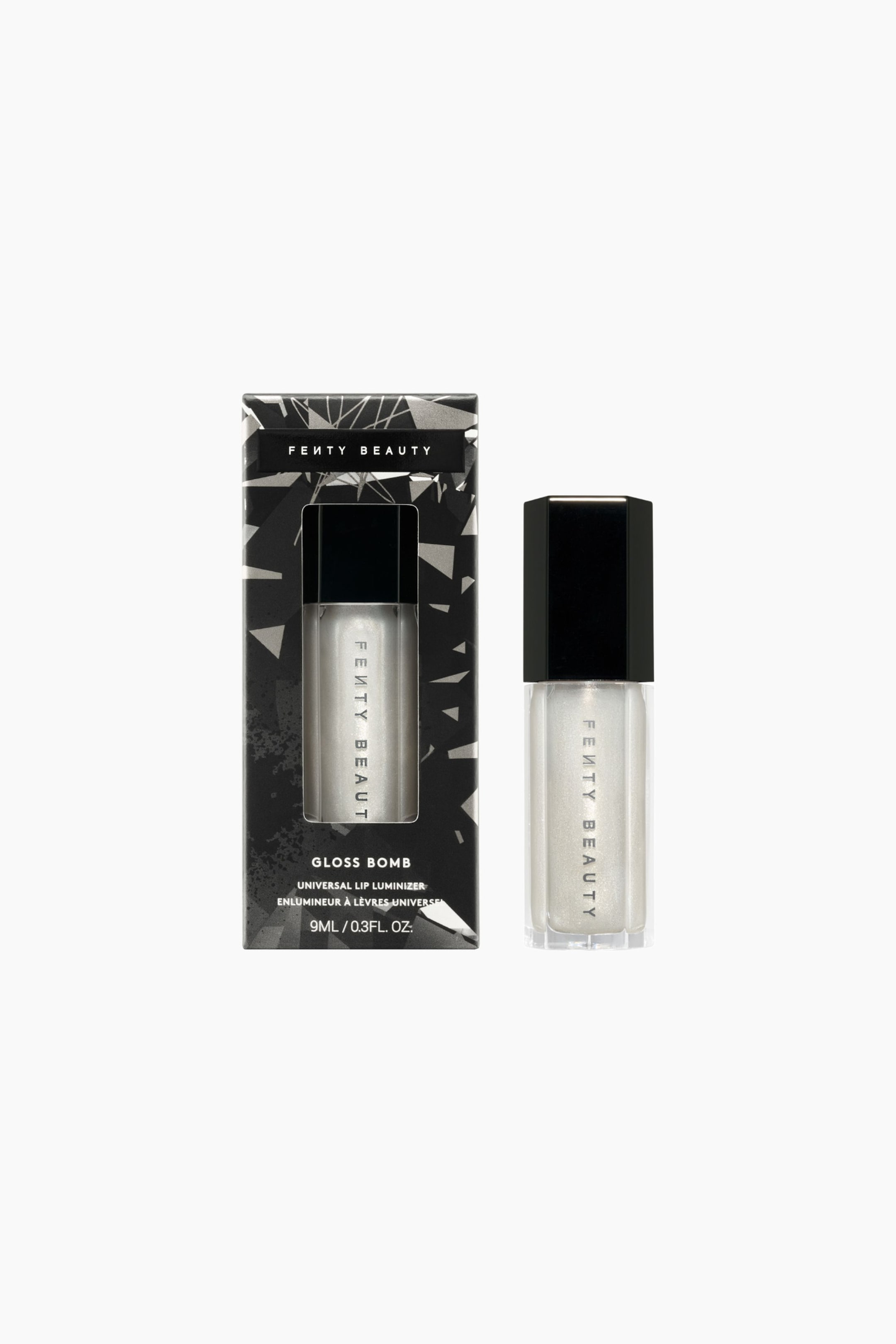 Visa större bild: Limited Edition Gloss Bomb Universal Lip Luminizer står upprätt bredvid sin förpackningsask och har en genomskinlig sexkantig flaska fylld med ett skimrande pärlemorskimrande vitt gloss, toppad med en svart sexkantig kork. Den svarta rektangulära förpackningsasken till vänster har ett geometriskt silvermönster och ett utskuret fönster som visar produkten inuti.