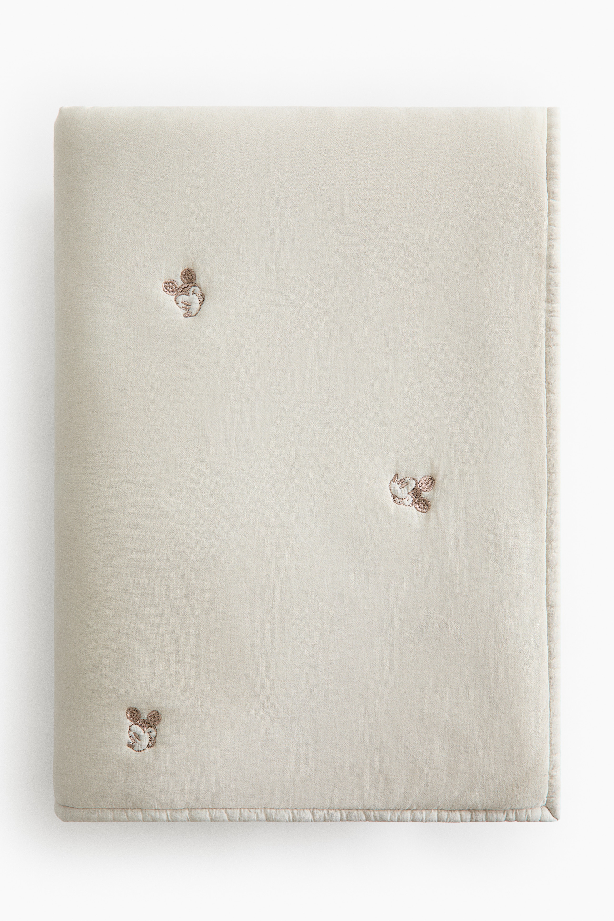 A lightly padded cream bedspread in a cotton weave features small, scattered embroidered motifs. The bedspread is folded back at the top to reveal a striped sheet underneath, while a matching cream pillow with the same embroidered details rests at the head of the bed.