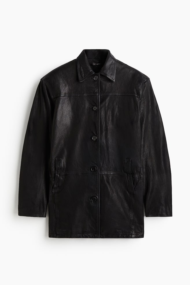 A straight-fit black leather coat is featuring a classic collar and a front button closure with five dark buttons. The coat is also displaying a horizontal front yoke seam, structured shoulders, and two vertical welt pockets on the lower front. - 1