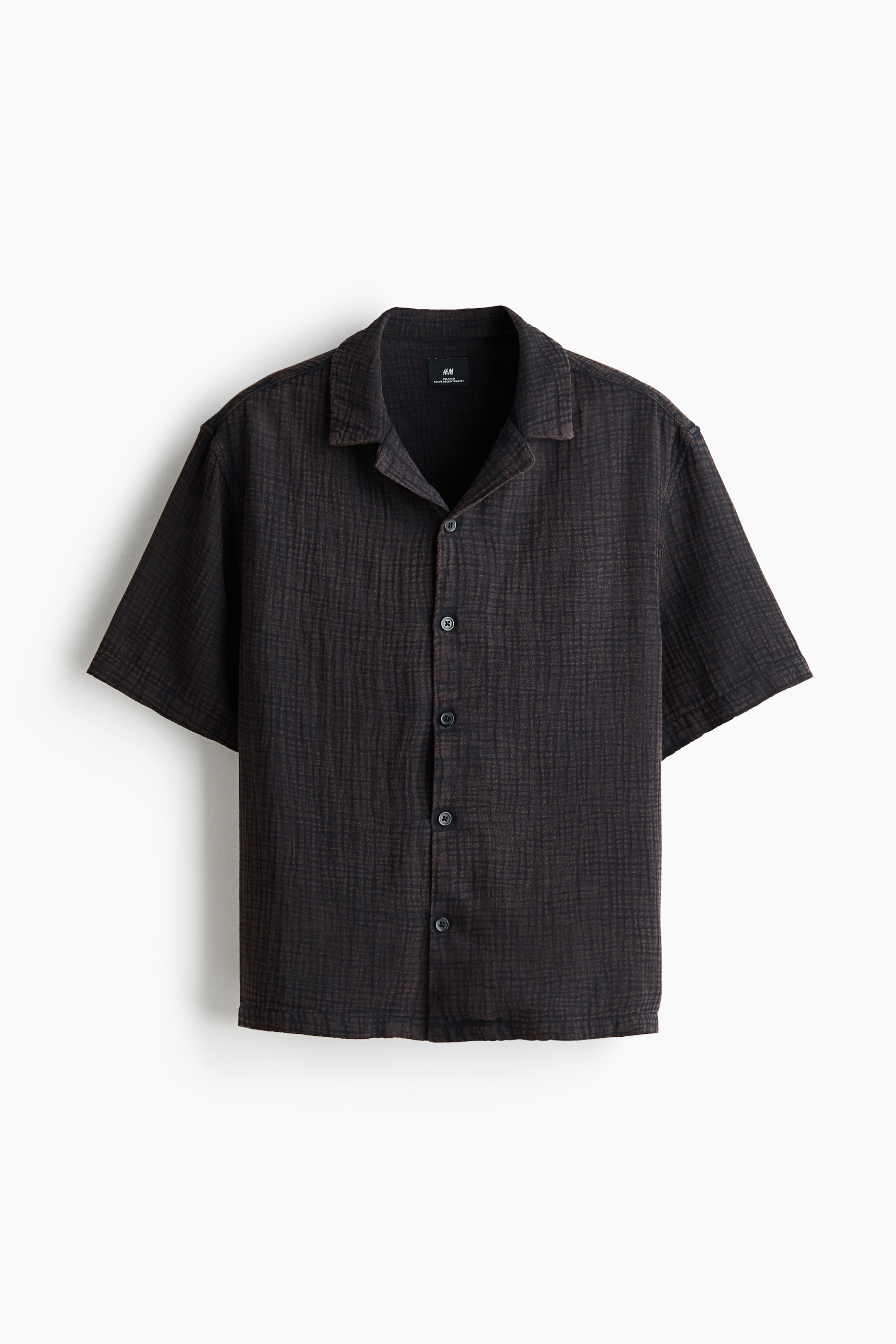 View larger image: A dark short-sleeved shirt is presented front-facing, featuring a textured, crinkled fabric with subtle grid lines. It is designed with a Cuban collar and a full button-front closure, secured with dark, round buttons.