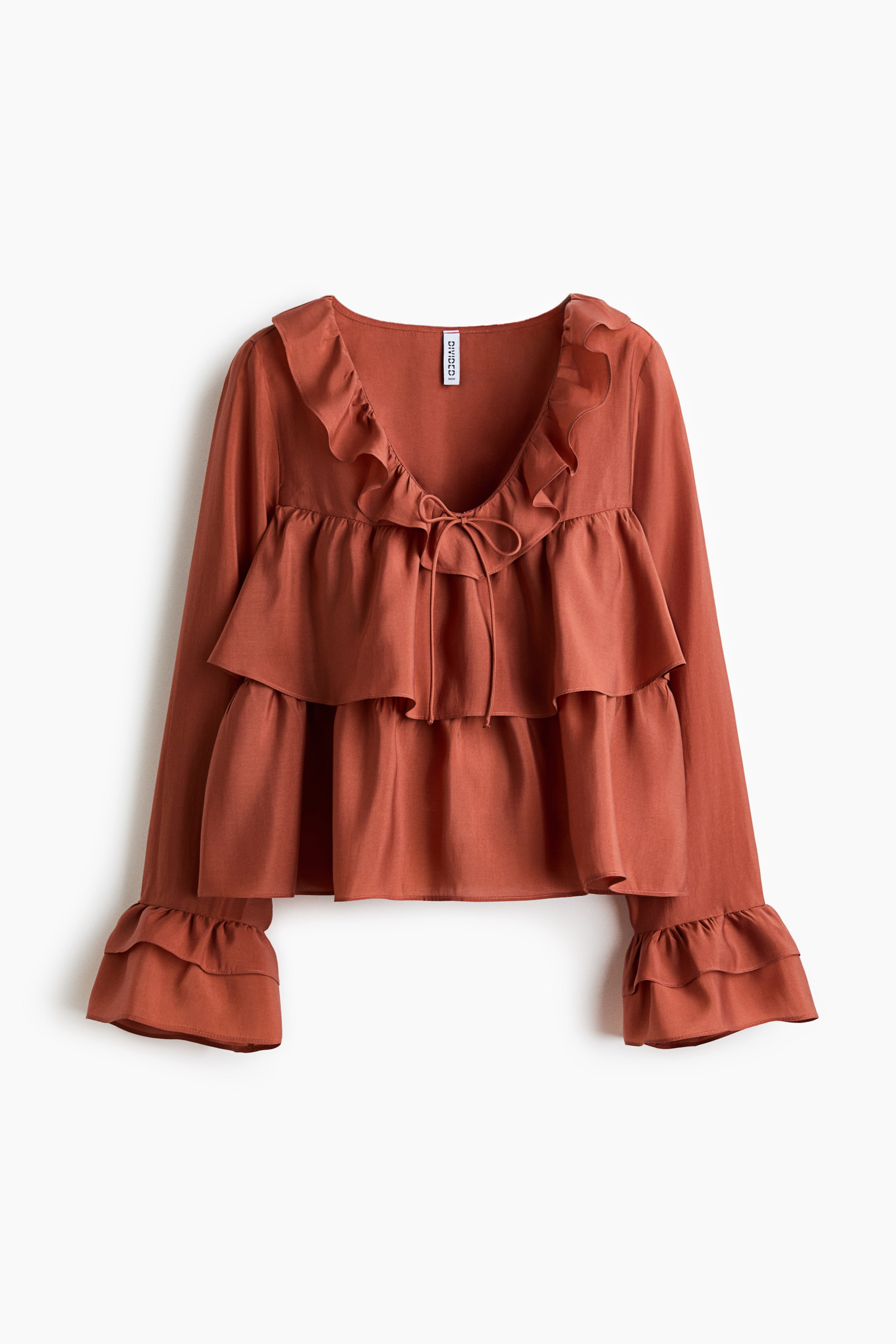 View larger image: A rusty orange blouse shown from the FRONT, featuring a sheer weave and a V-shaped neckline with frill trim and narrow ties at the front. It also has a wide frill trim around the bust and at the hem for a tiered look, along with long sleeves finished with double frill trims at the cuffs.