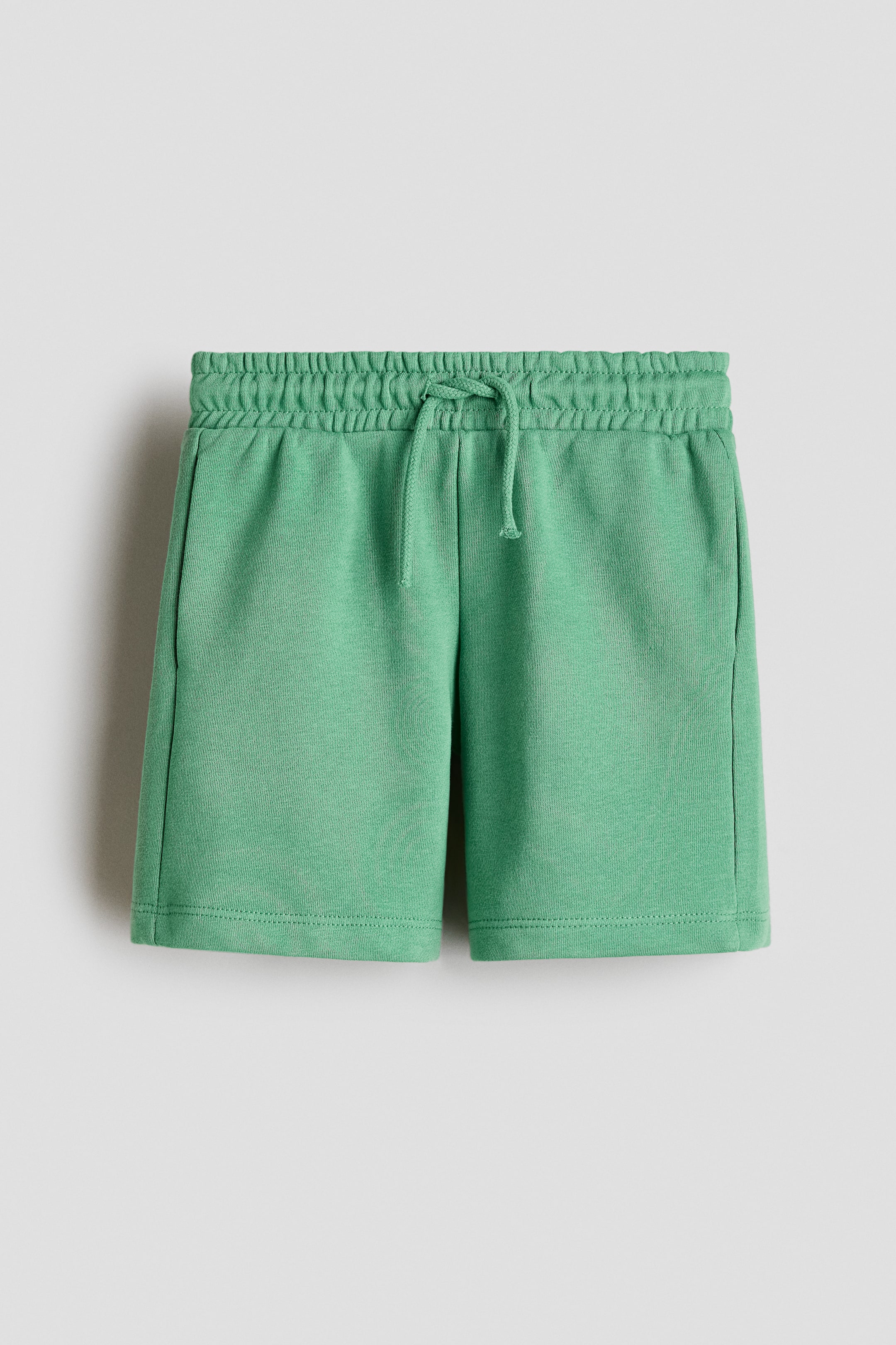 View larger image: Green shorts are presenting their front, featuring an elasticated waistband with a tied drawstring. Side seam pockets are visible on both sides.