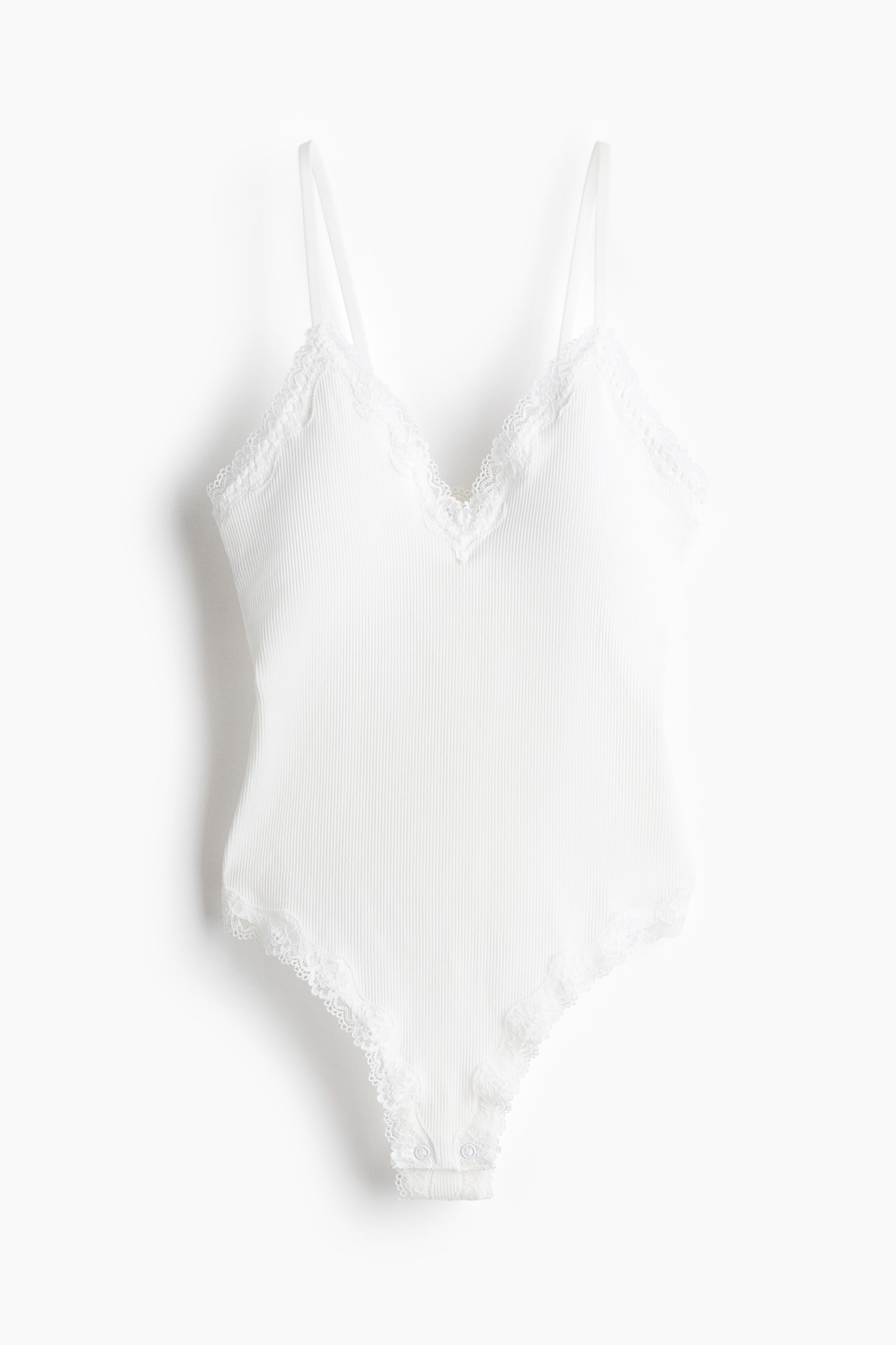 Ampliar la imagen: Un bodysuit blanco acanalado se muestra de FRENTE, con escote en V y ribete de encaje blanco en el escote y en las aberturas de las piernas. Está diseñado con tirantes delgados y ajustables, y se observan broches a presión en la entrepierna.