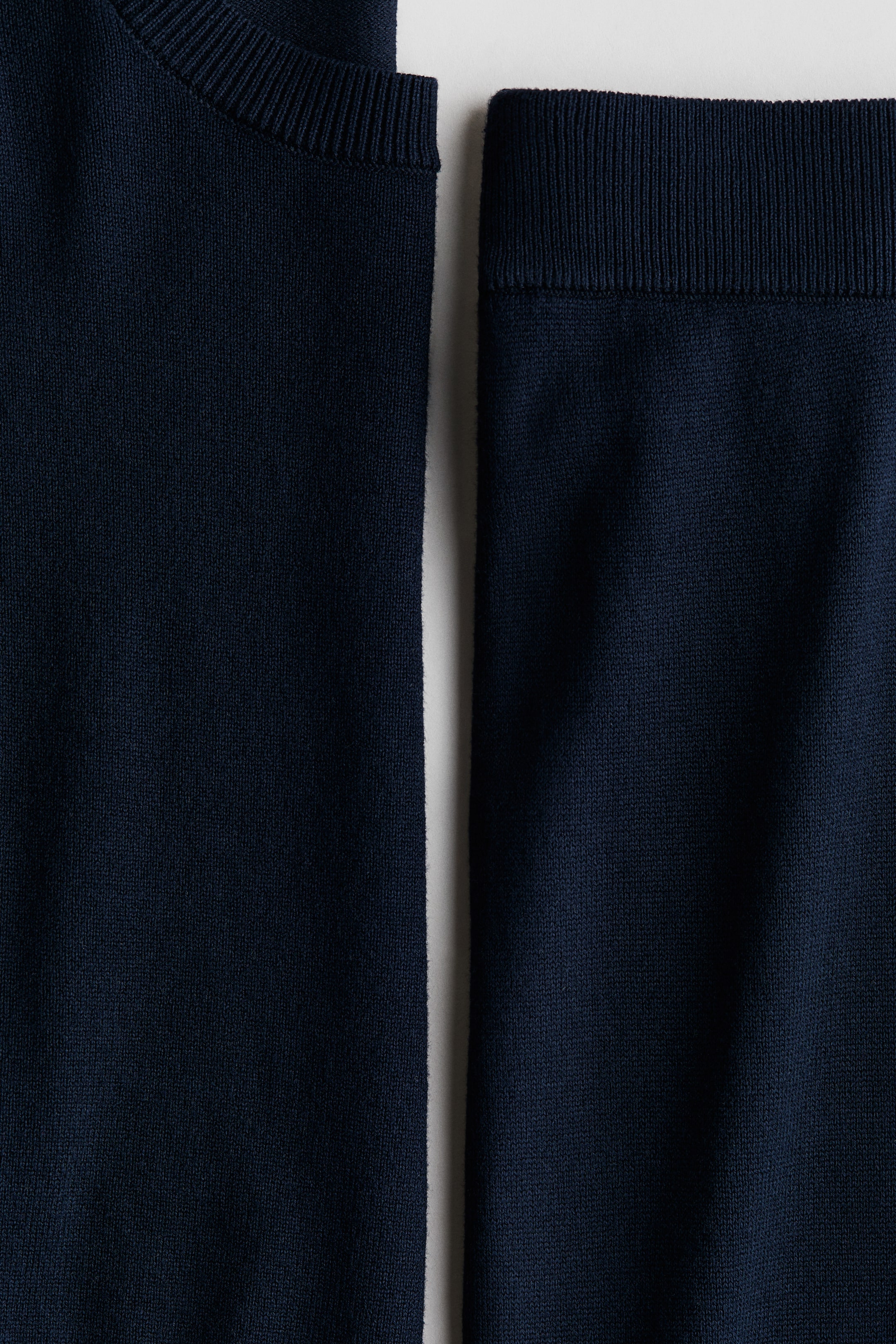Größeres Bild ansehen: Ein dunkelblaues Feinstrick-Set zeigt einen Pullover mit rundem, geripptem Ausschnitt und Jogginghosen mit geripptem, elastischem Bund.