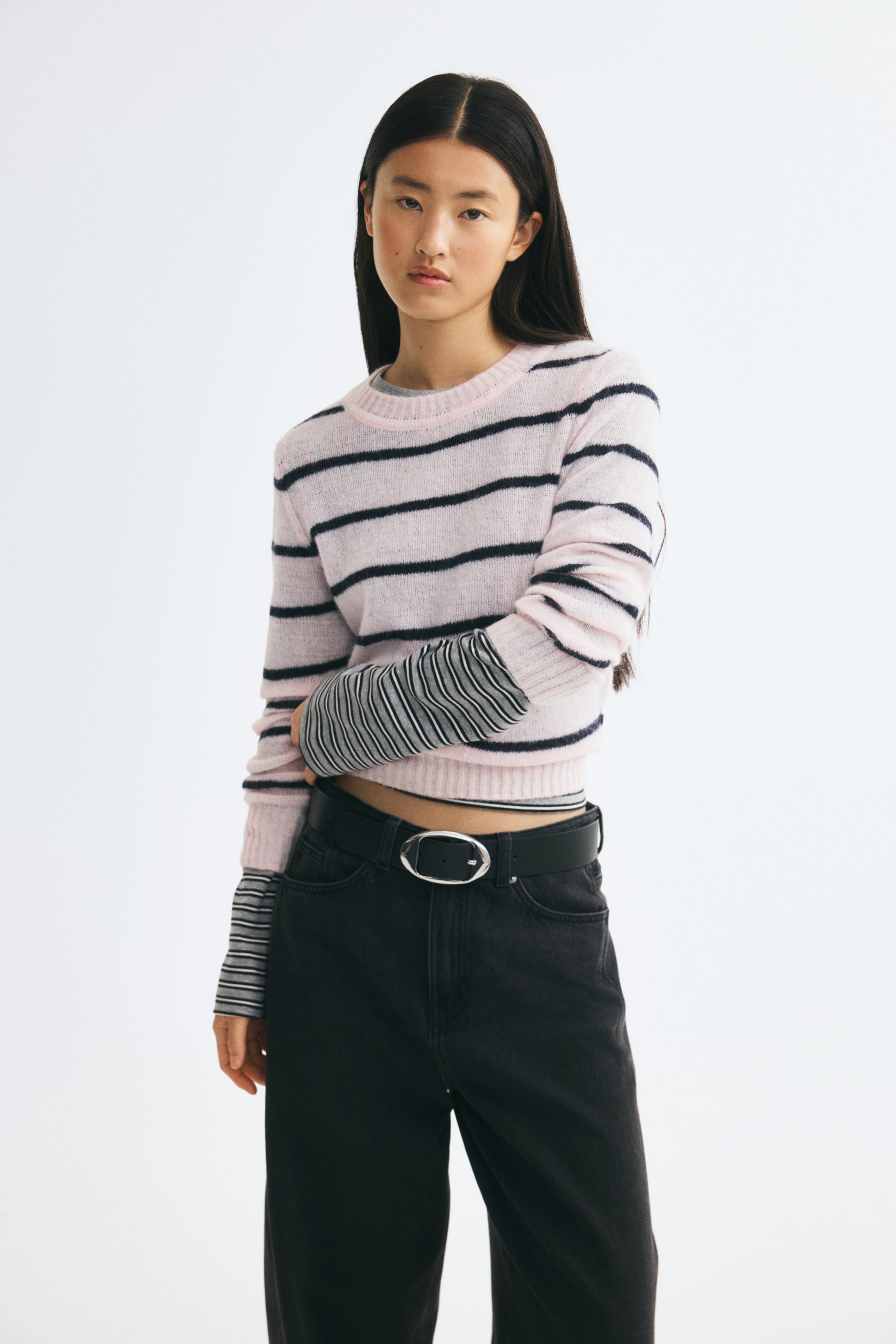 View larger image: A fitted, light pink sweater with horizontal black stripes is shown in a front view, styled over a grey and black striped long-sleeve top. The sweater features a ribbed crew neck, ribbed cuffs, and a ribbed hem, and is paired with black denim jeans.