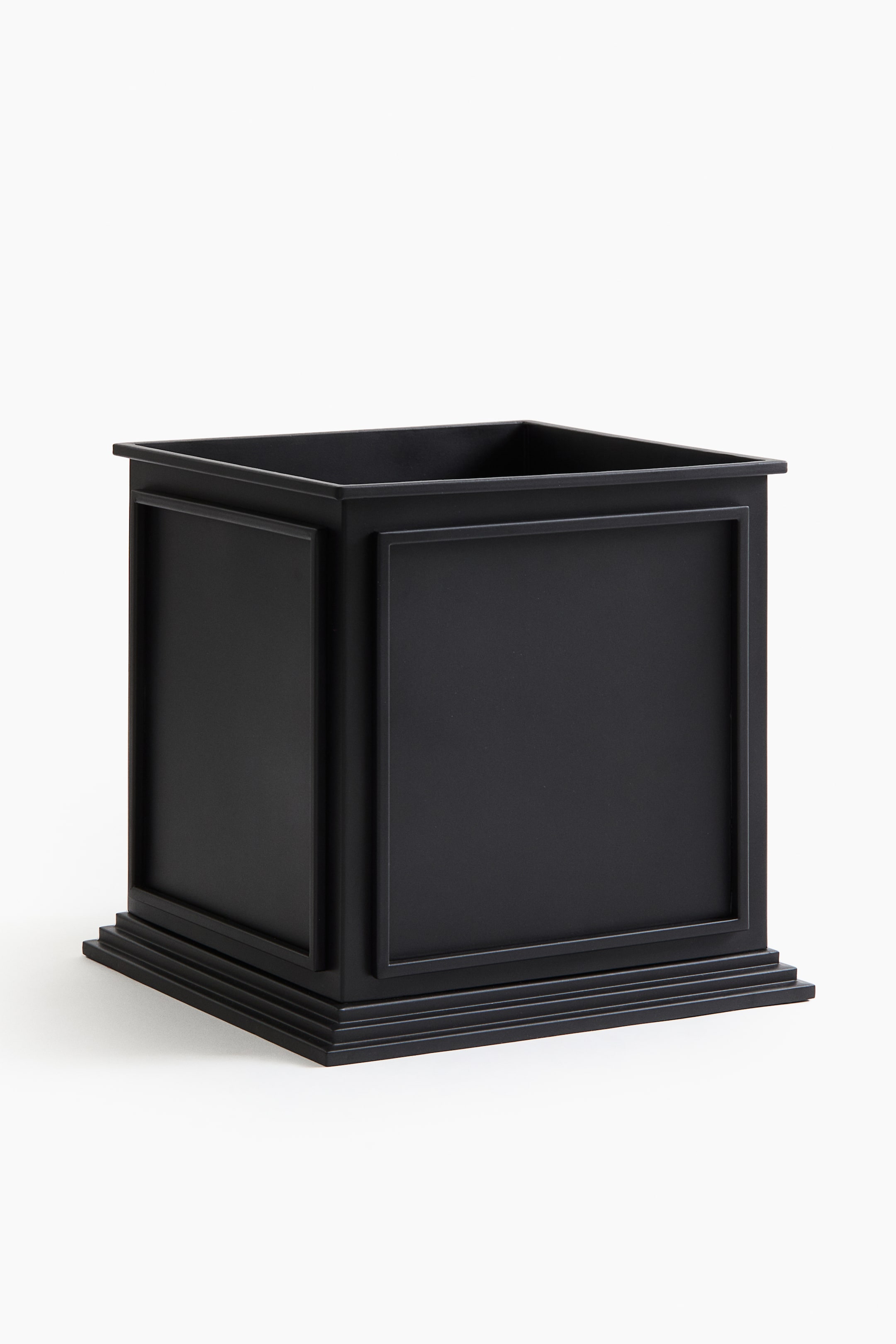 Zobrazit větší obrázek: Velký černý kovový květináč ukazuje svůj čtvercový tvar z mírného předního úhlu, odhalující otevřený vrch a dvě strany. Každá strana je opatřena vyvýšeným obdélníkovým panelem a širší základna je zdobena několika stupňovitými horizontálními liniemi.