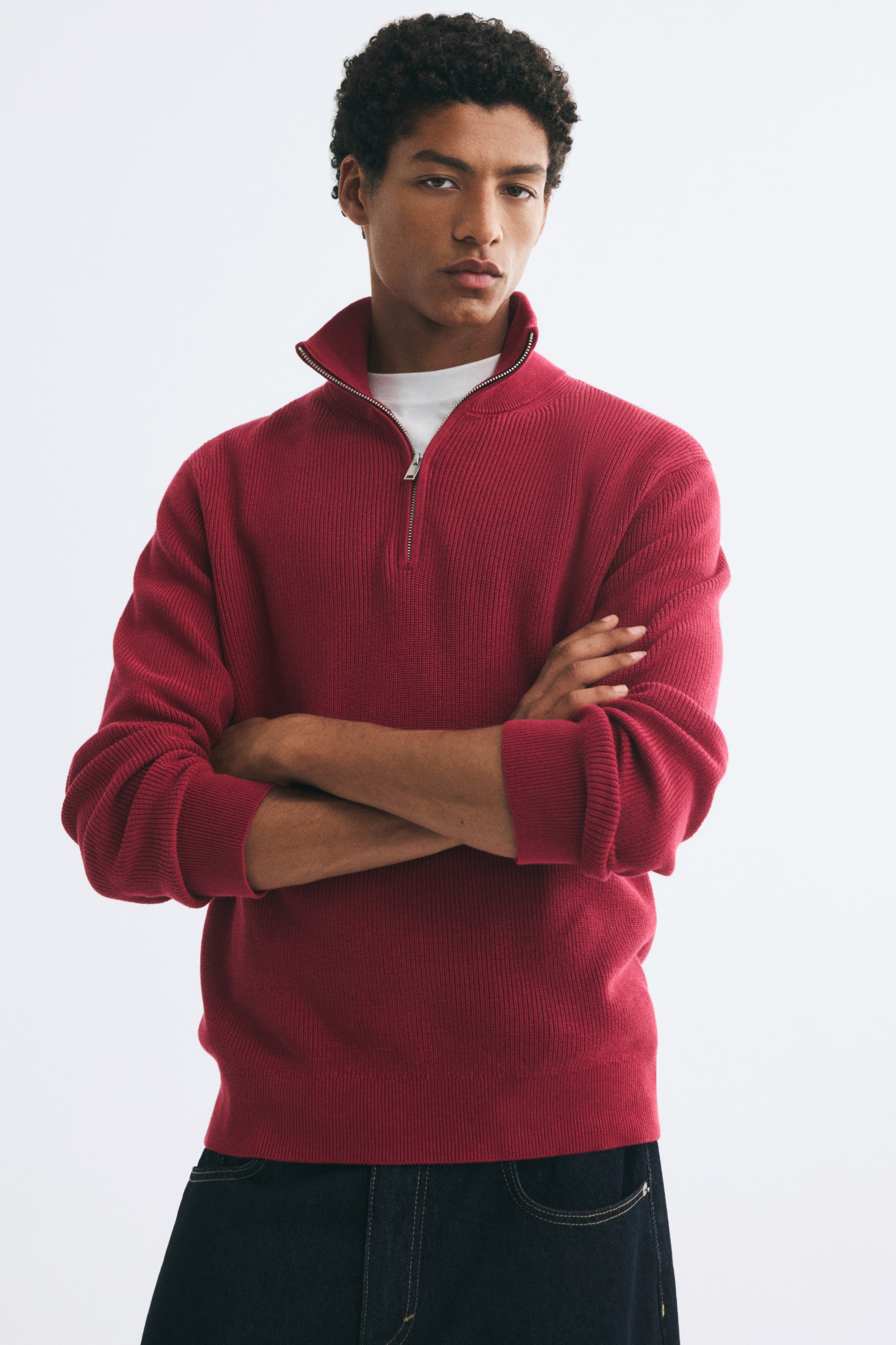 View larger image: A red, rib-knit cotton sweater featuring a stand collar with an open half-zip is being worn by the model with arms crossed. The sweater is layered over a white crew-neck T-shirt and paired with dark denim jeans.