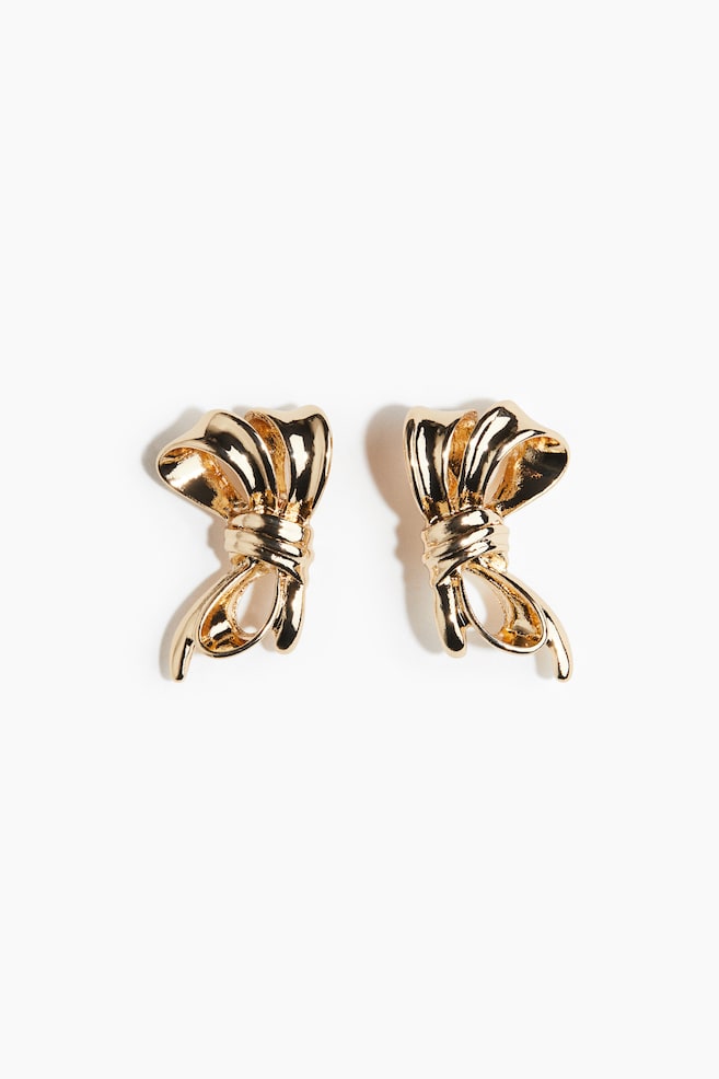 Two gold-toned bow-shaped earrings are presented from the front. Each earring is sculpted with a central knot, two upper loops, and two lower trailing ends. - 1