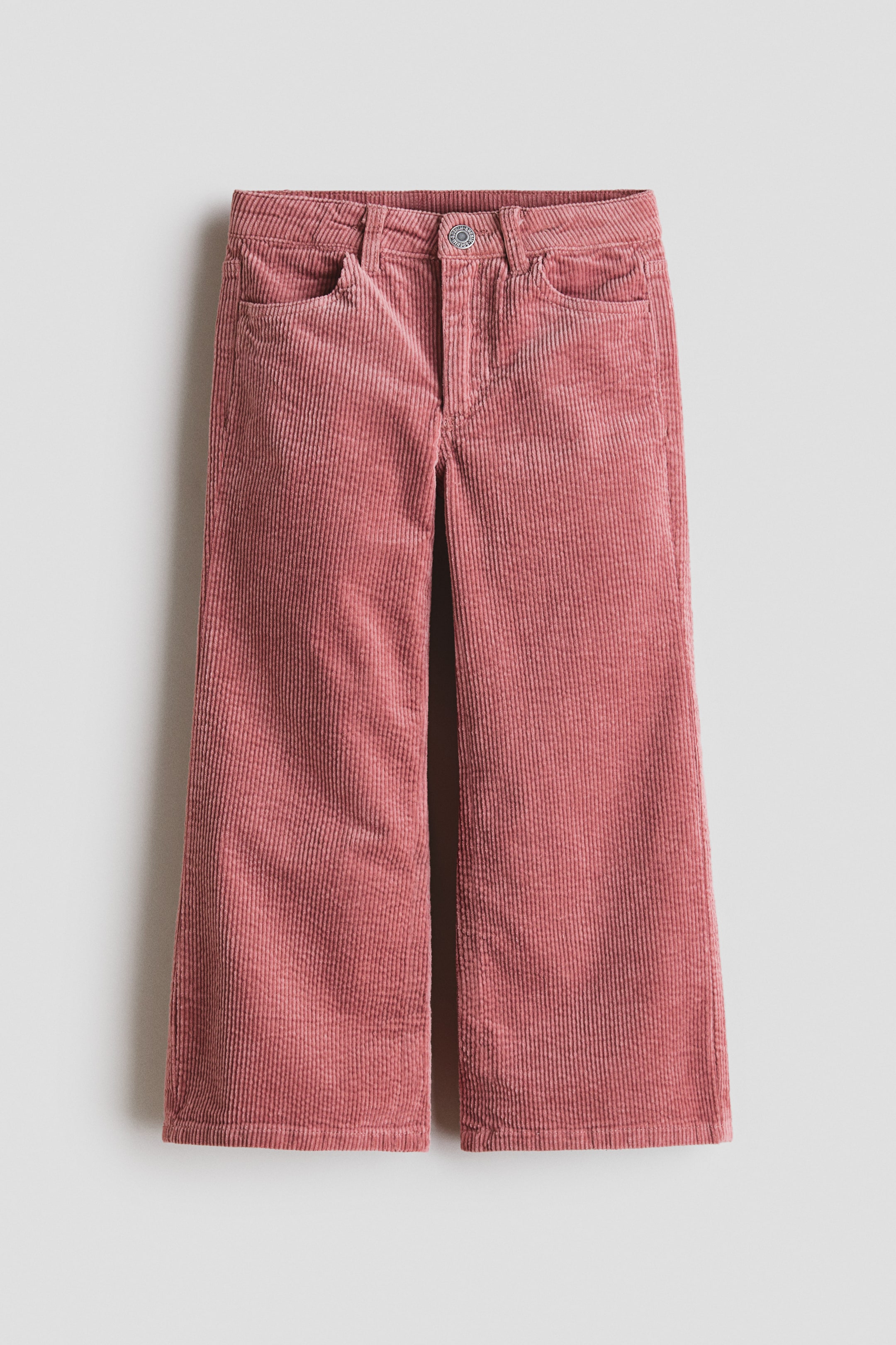 Agrandir l'image: Un pantalon large en velours côtelé rose est présenté de face, avec des côtes verticales bien marquées, une ceinture plate avec passants pour ceinture, une fermeture à un seul bouton métallique et deux poches avant en biais.