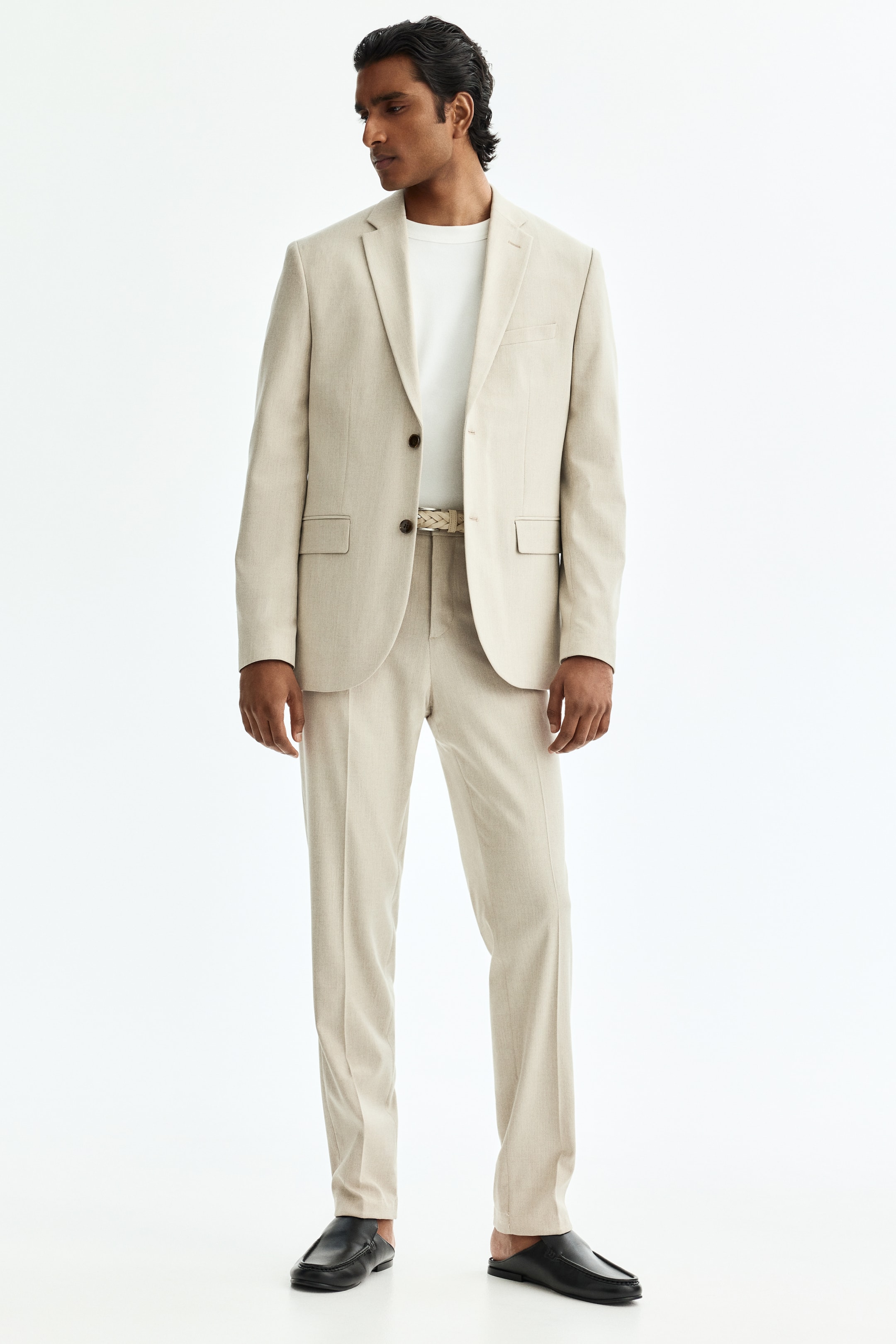 Visualizza immagine più grande: Pantaloni del completo beige chiaro, realizzati in un tessuto morbido, sono presentati frontalmente, mettendo in evidenza una vestibilità slim che aderisce alle linee del corpo. Presentano pieghe che scendono lungo la parte anteriore delle gambe e tasche laterali visibili, con una cintura intrecciata indossata nella cintura.