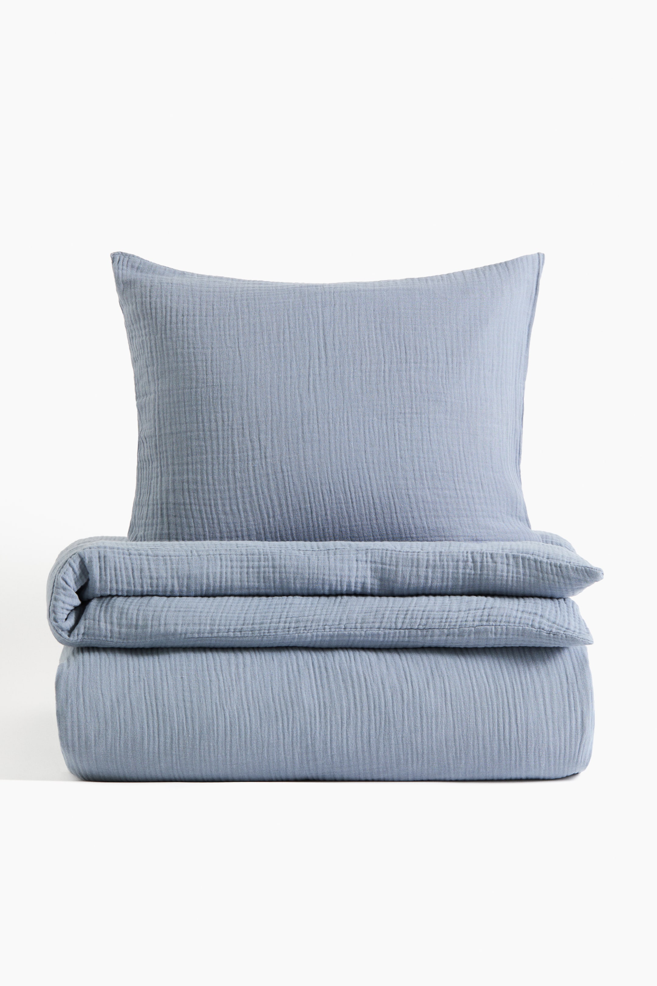 Ver imagen más grande: Un juego de funda nórdica azul claro muestra una textura de muselina arrugada. El conjunto incluye una funda de almohada vertical y una funda nórdica a juego que está cuidadosamente doblada debajo.