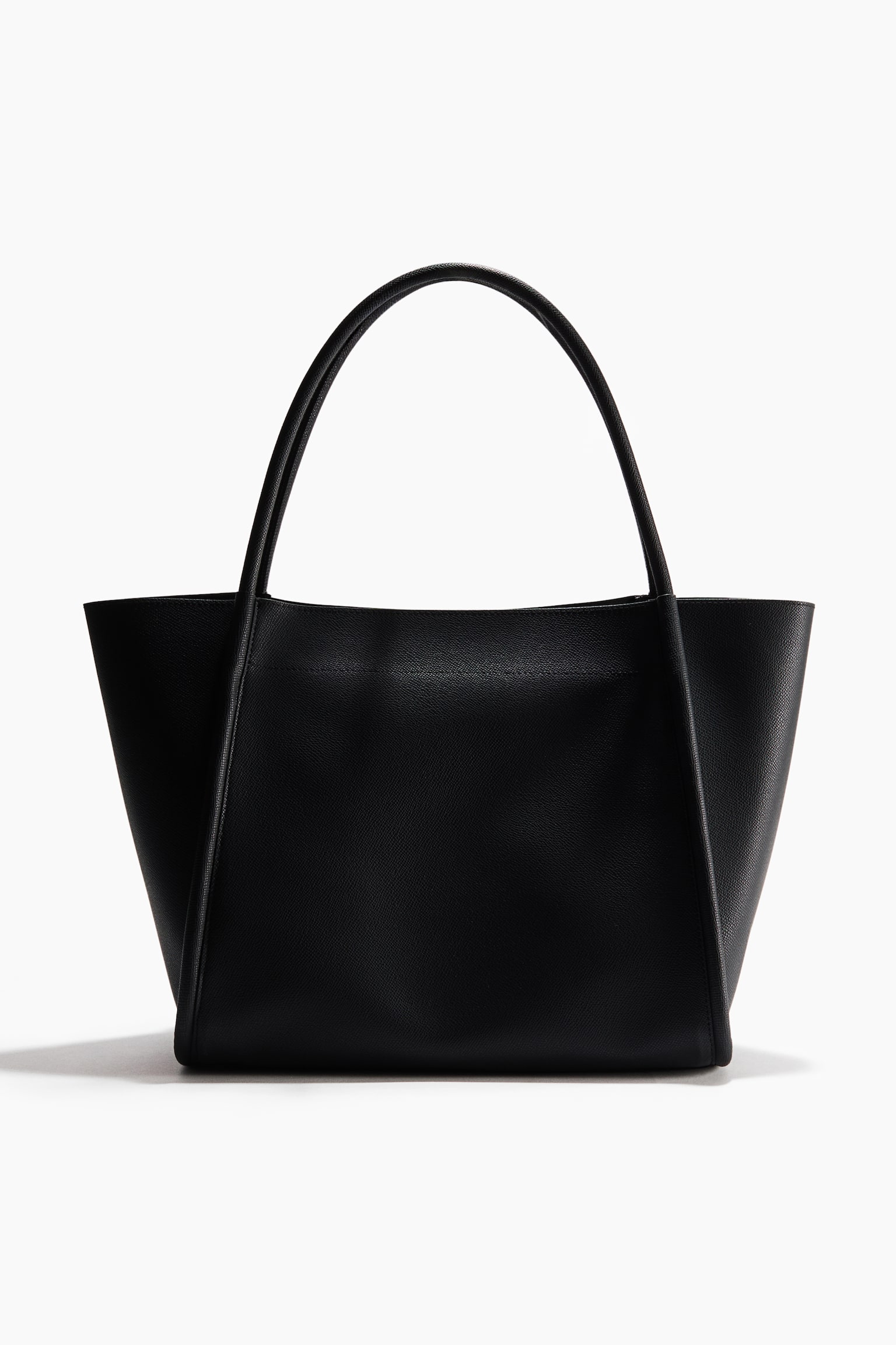 A black shopper bag in textured coated fabric stands upright, facing front, showcasing a structured trapezoidal silhouette with flared sides. It features two rounded top handles that extend down the front panel as structural trim.