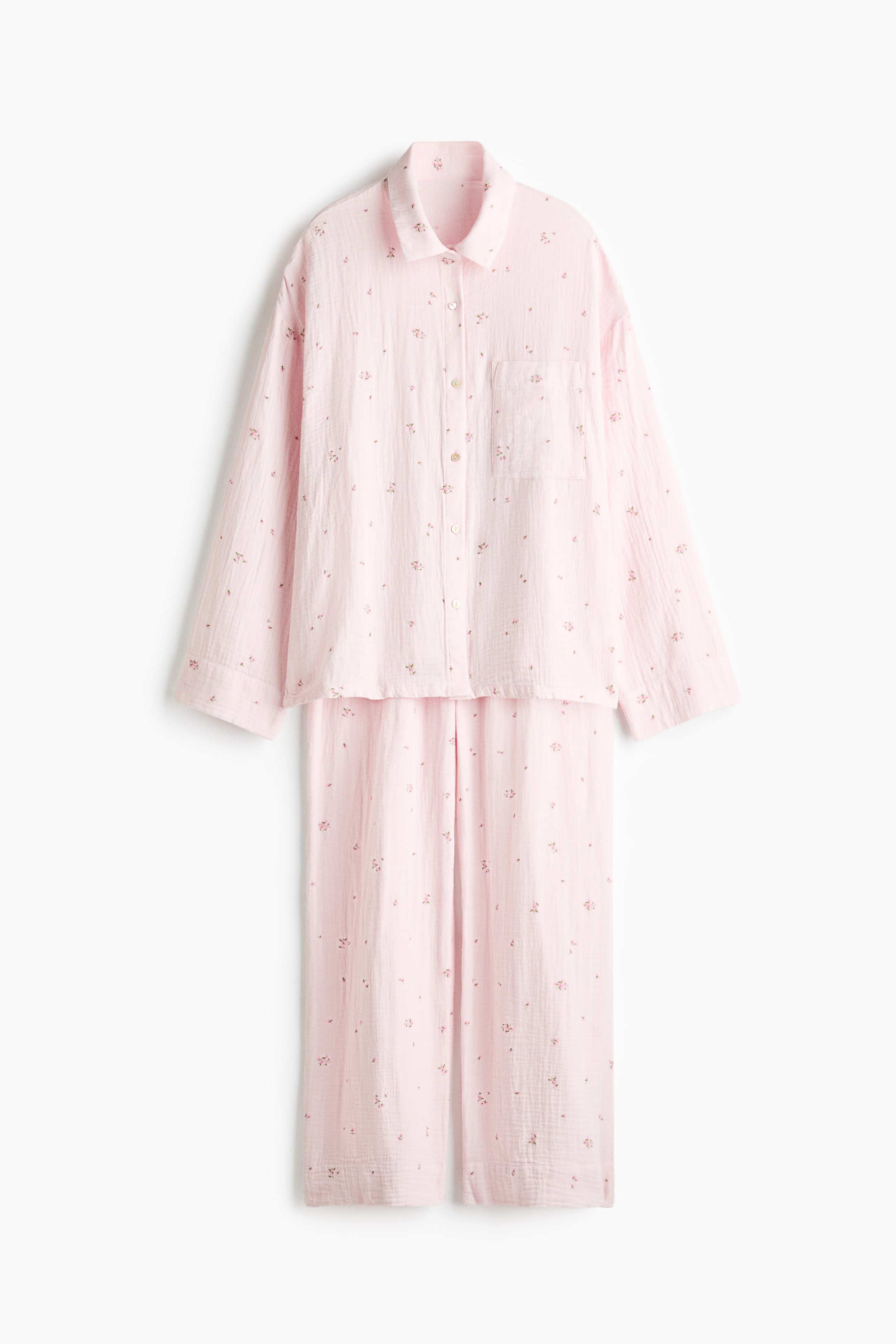 Agrandir l'image: Un ensemble de pyjama en mousseline de coton rose pâle, orné d’un délicat motif floral, est présenté de face. L’ensemble comprend une chemise à manches longues avec col, ouverture boutonnée sur le devant, épaules tombantes et poche poitrine plaquée, assortie d’un pantalon droit coordonné.