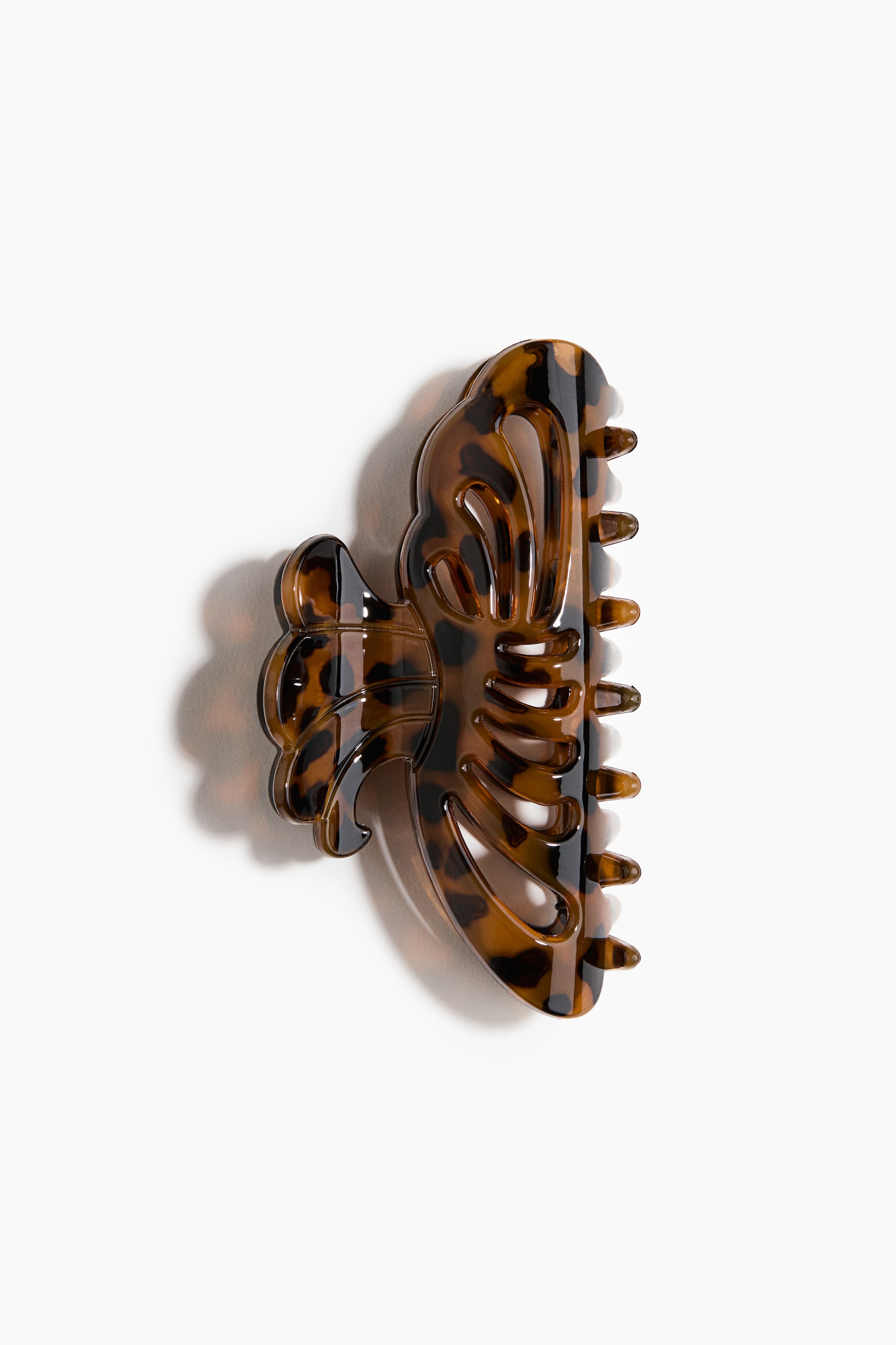 View larger image: A hair claw made of shiny tortoiseshell plastic features a curved, openwork design and is shown in side profile with visible interlocking teeth.