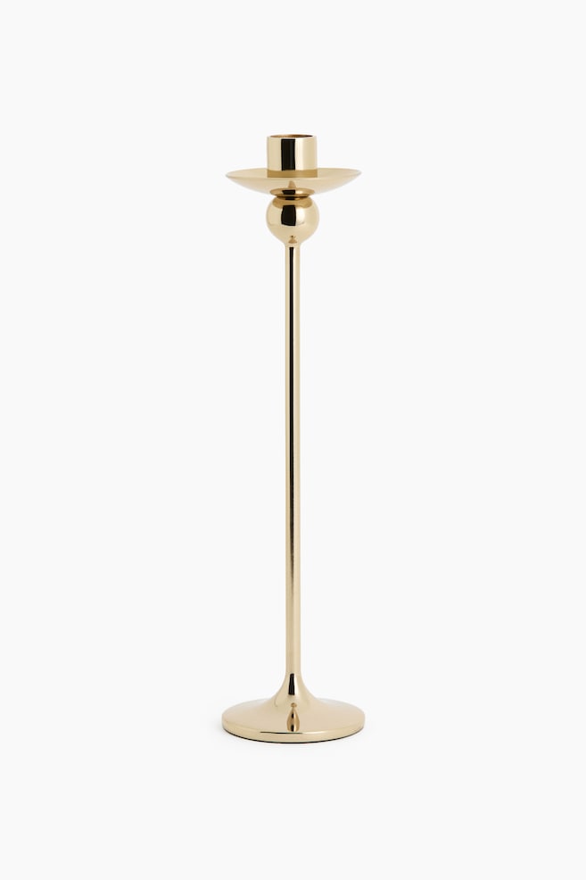 A tall candlestick in a polished gold-tone finish is shown from the front, featuring a sleek, slender stem rising from a flared circular base. The design includes a spherical detail positioned directly below a wide, shallow drip pan and a cylindrical candle holder at the top. - 1