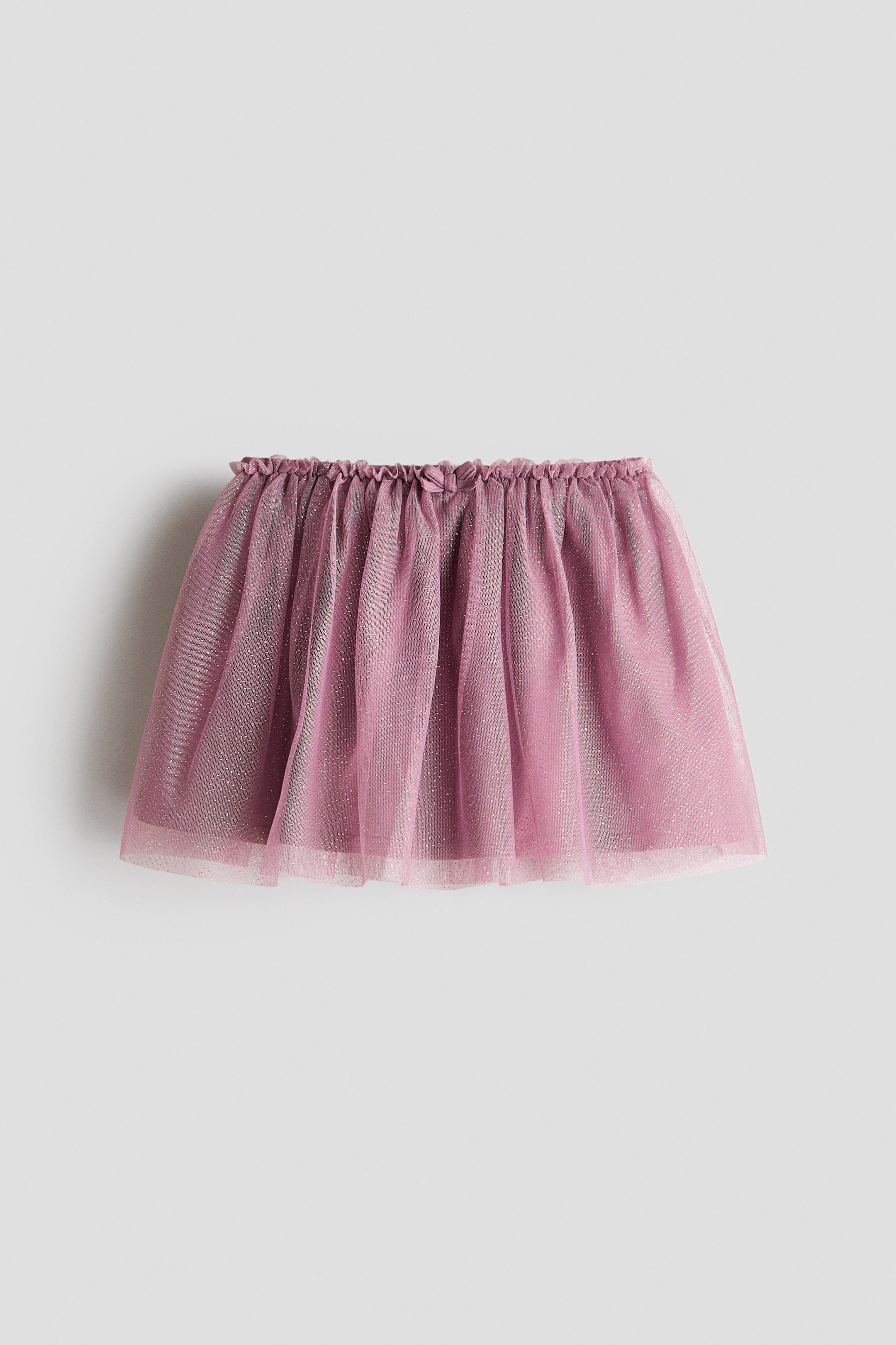 View larger image: A dusky pink flared skirt crafted from sheer, glittery tulle, featuring an elasticated, ruffled waistline adorned with a decorative bow at the front. A darker lining is subtly visible beneath the sheer layer.