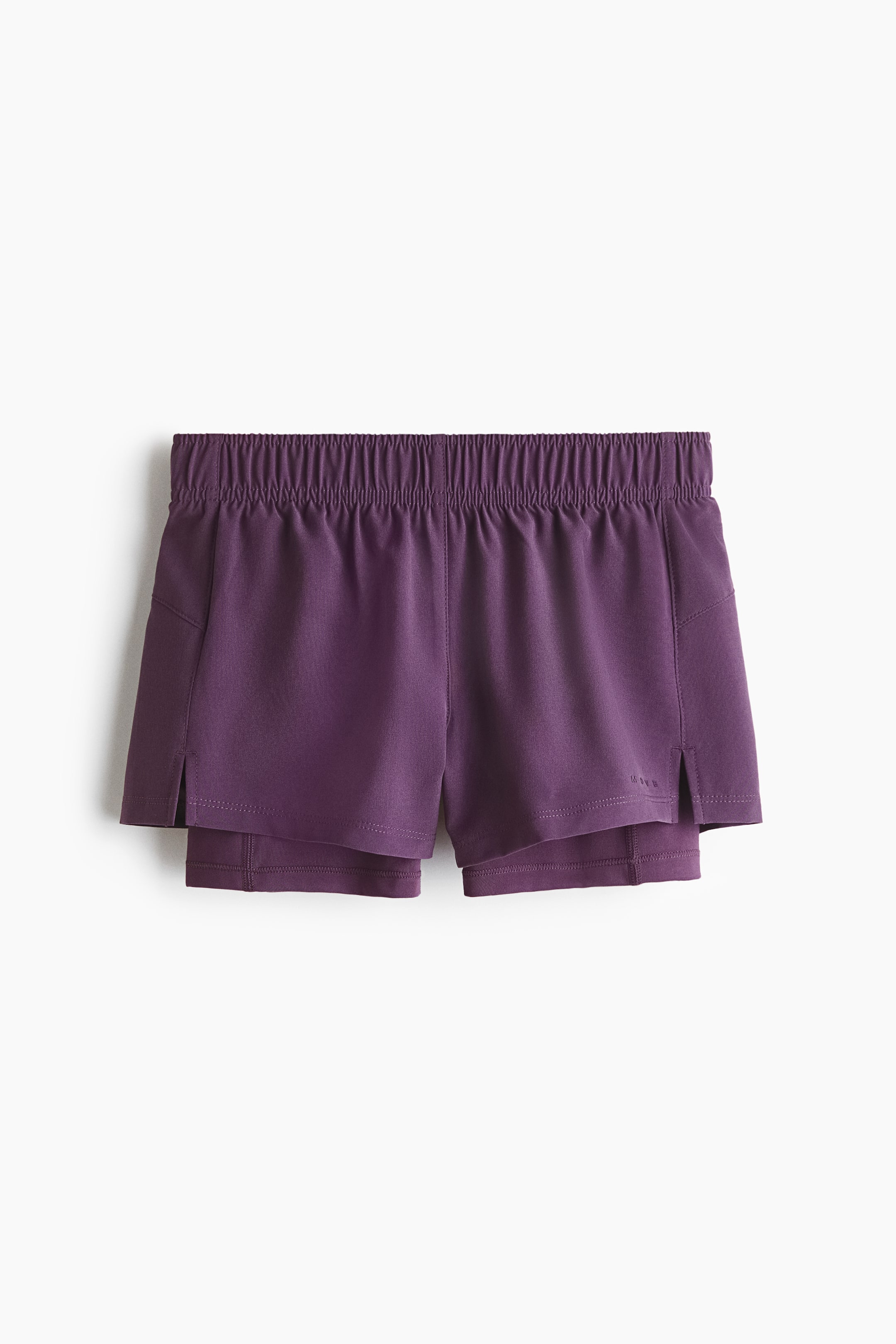 Grösseres Bild ansehen: Violette, doppellagige Laufshorts sind nach vorne gerichtet und zeigen einen elastischen, gerafften Bund. Die äußere Schicht verfügt über seitliche Schlitze an den Säumen und eine schräge Tasche auf der linken Seite, die eine längere, eng anliegende innere Schicht darunter offenbart, mit einem dezenten 'H&M Move'-Logo, das am rechten Saum erscheint.