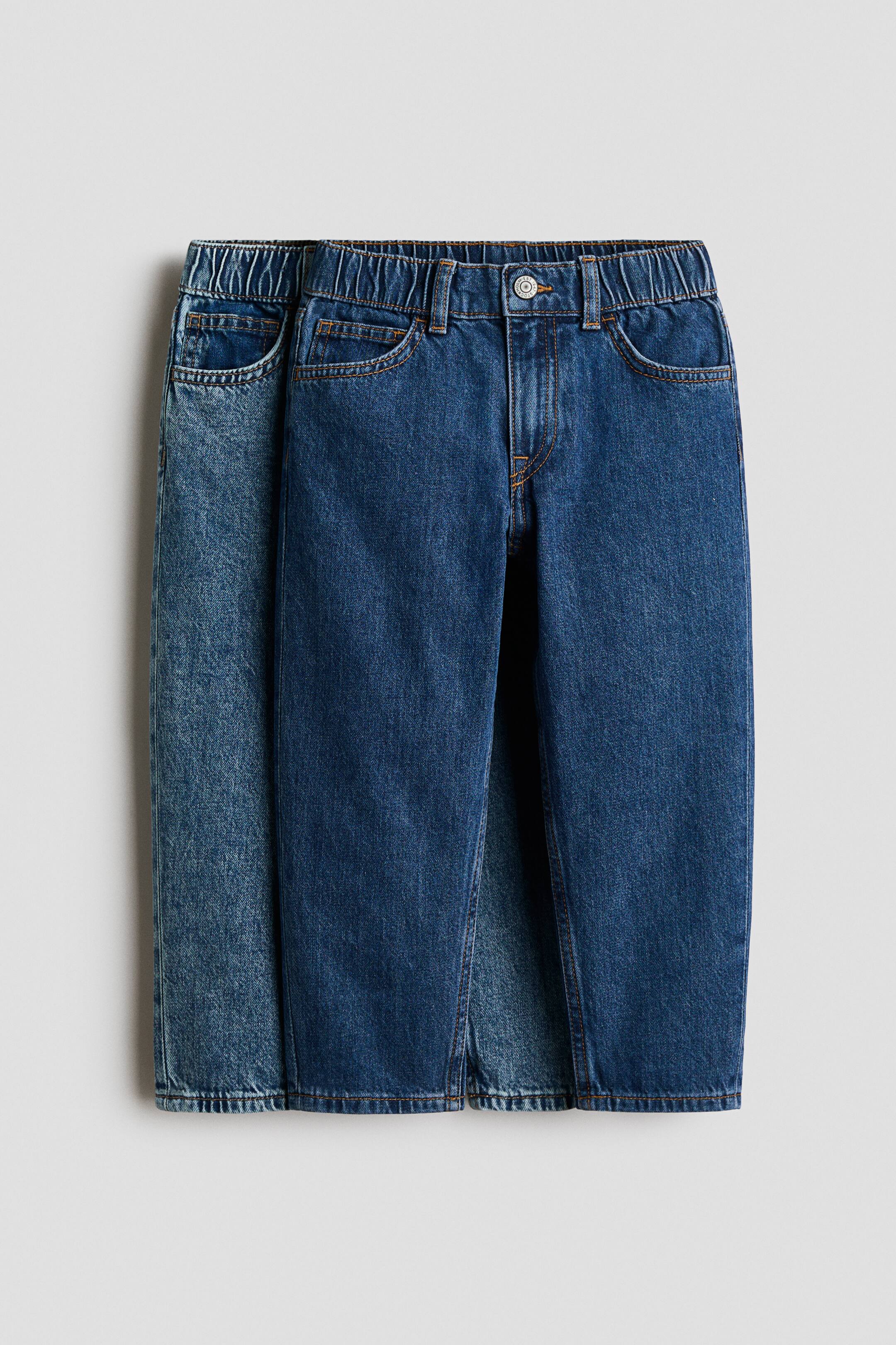 Grotere afbeelding bekijken: Twee paar 5-pocket jeans in gewassen katoenen denim zijn van voren te zien, met een donkerder blauw paar vooraan en een lichter blauw paar erachter. Beide modellen hebben een verstelbare, elastische tailleband met ritssluiting en drukknoop, en een loose fit ter hoogte van heup en dij met taps toelopende pijpen.