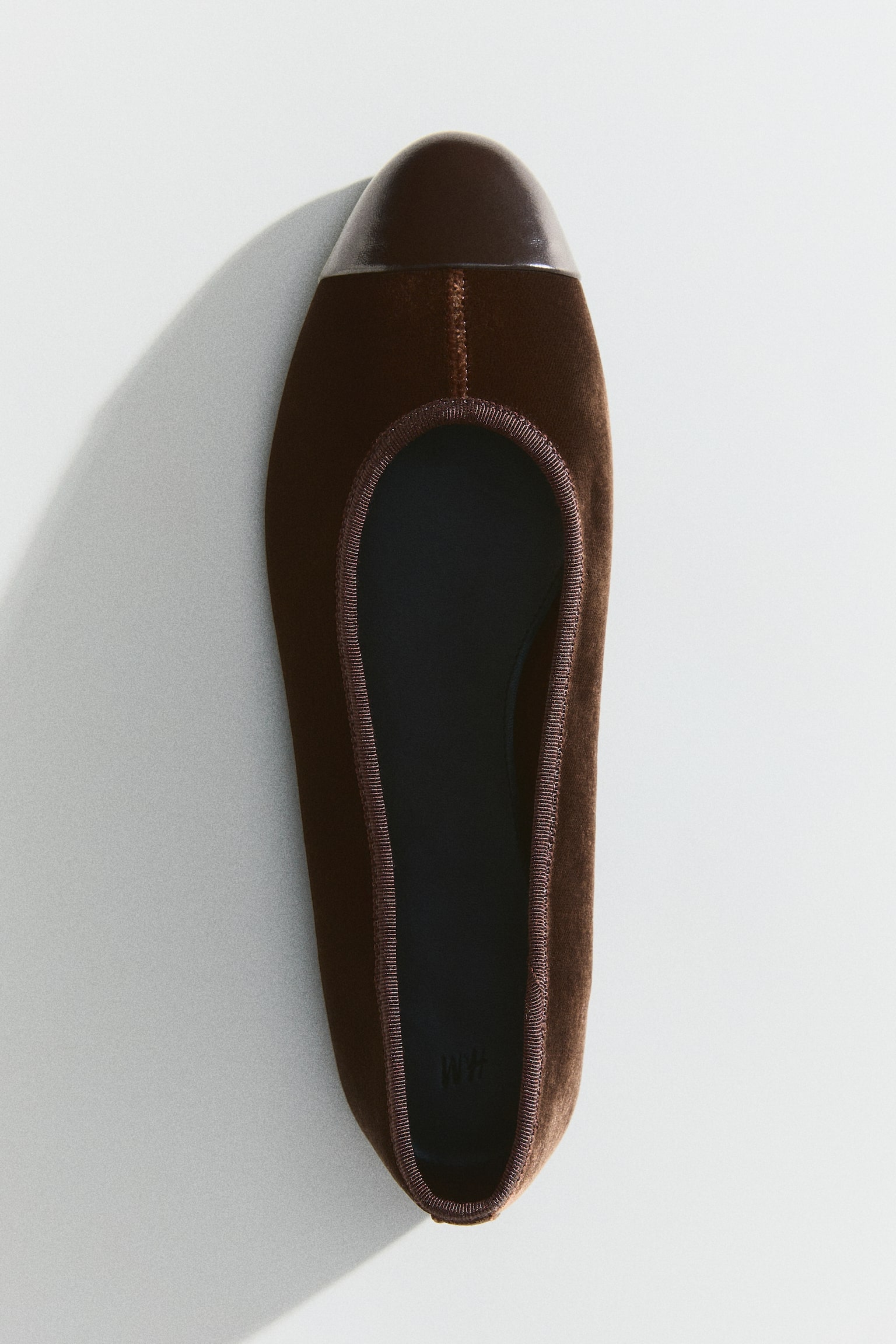 A pair of brown ballet flats is showcased, each shoe boasting velvet uppers and a rounded, dark brown patent leather toe cap. A slim brown ribbed trim outlines the opening, and a black inner sole rests inside. - 1