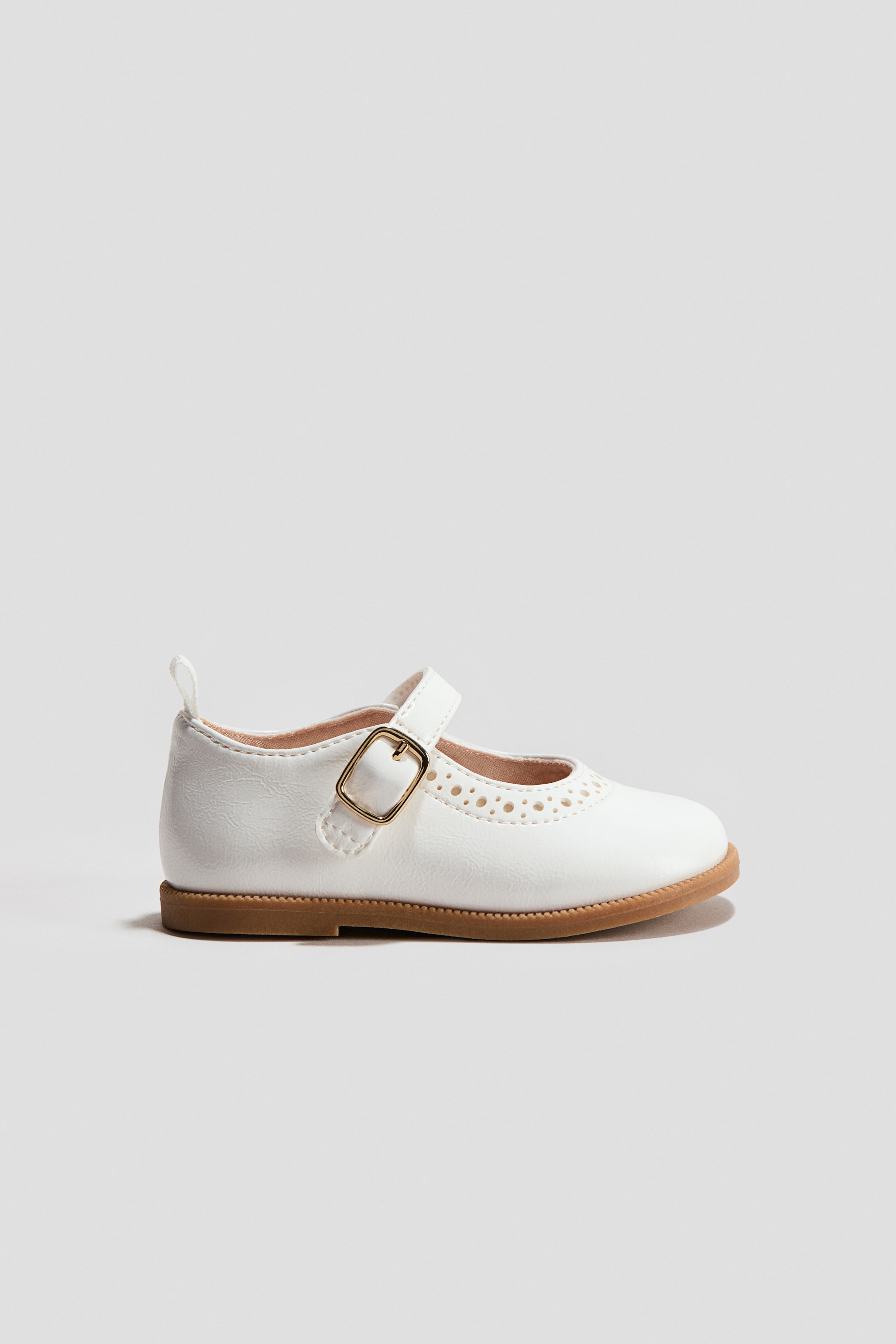 Ampliar la imagen: Zapato Mary Jane blanco, hecho de tela recubierta, con borde perforado en la parte delantera, correa en el empeine con hebilla dorada y suela marrón.