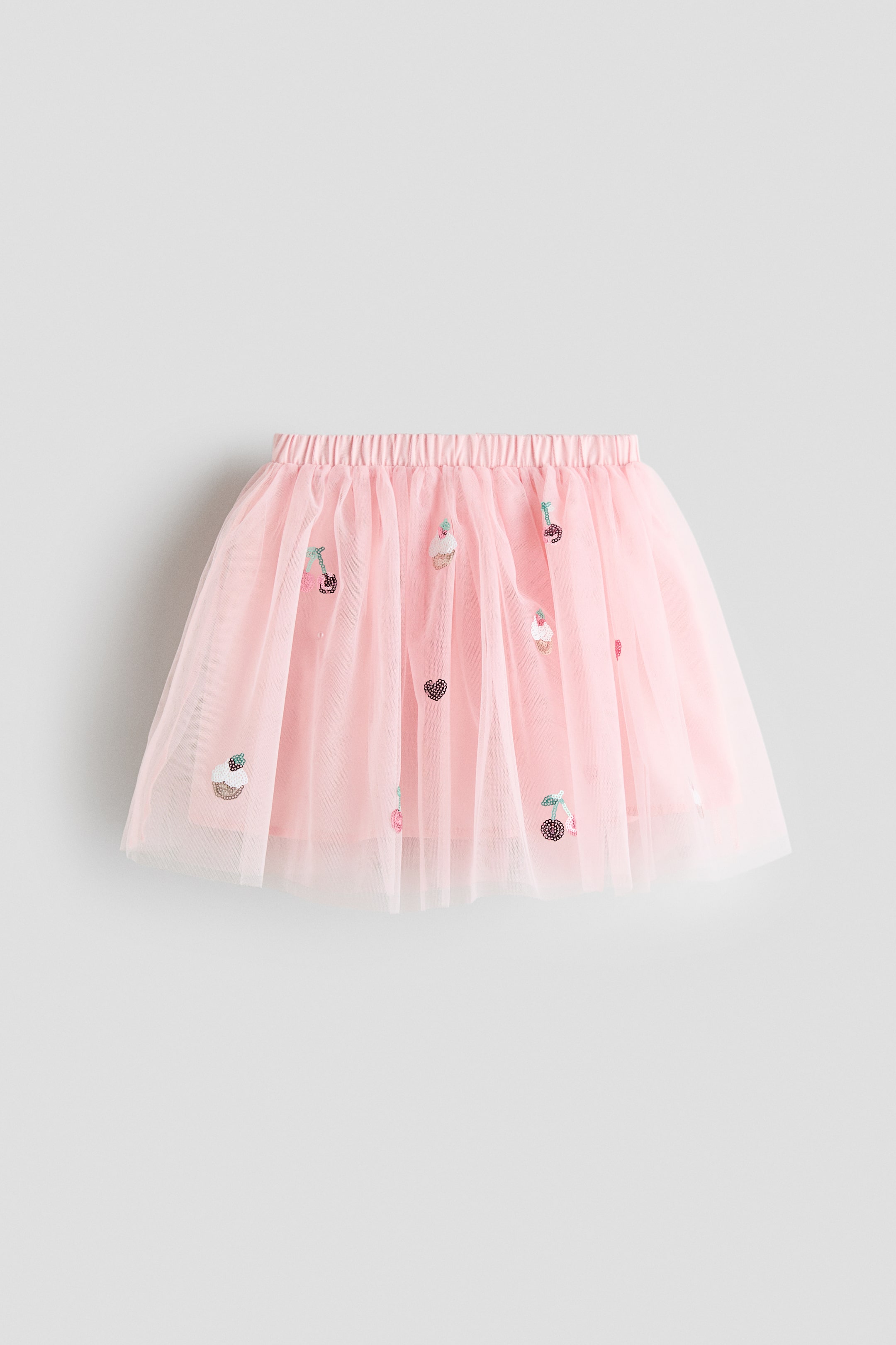 View larger image: A pink tutu skirt comes with an elasticated waistband and multiple layers of sheer pink tulle. Sequined cupcake, cherry, and heart motifs adorn its front.