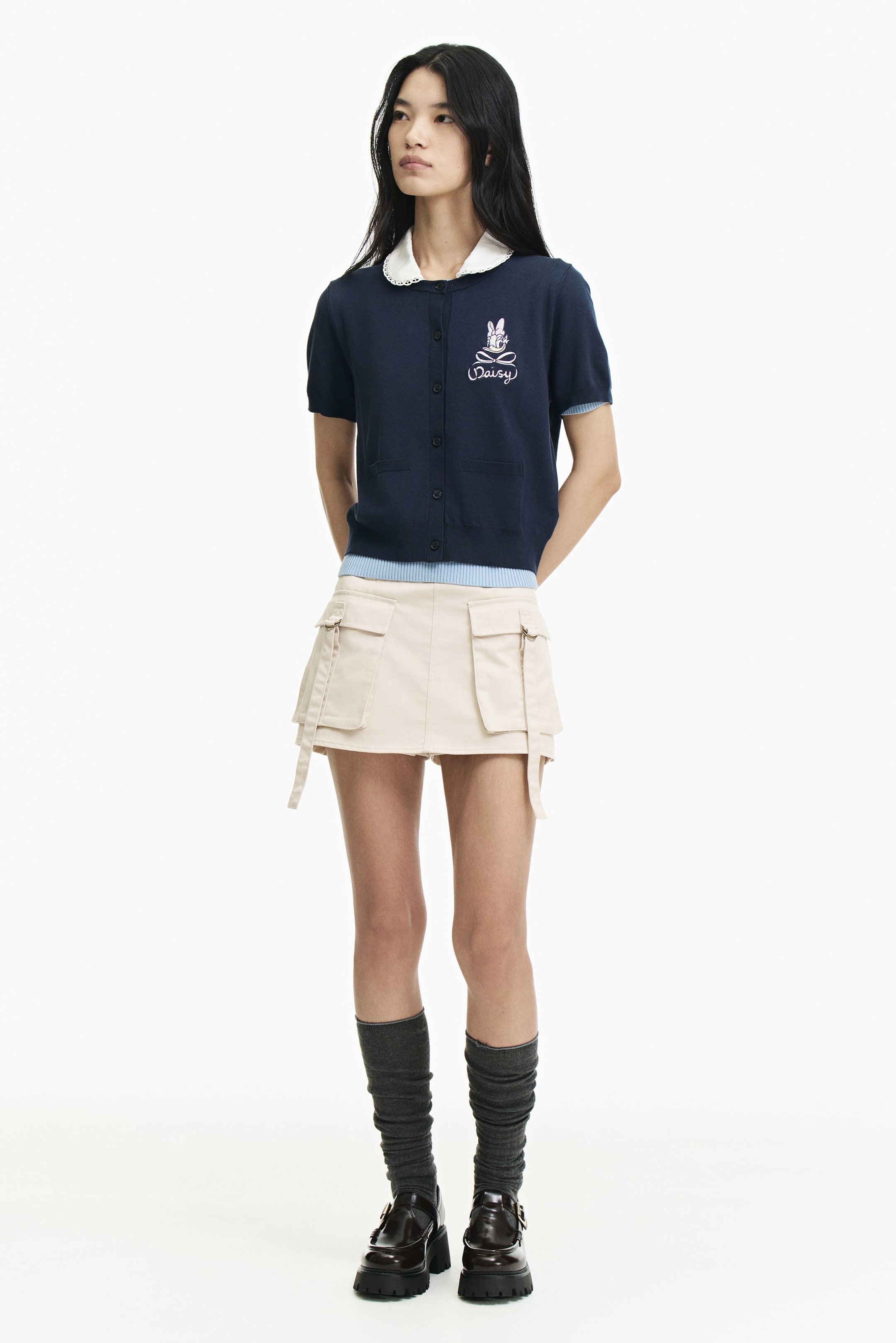 View larger image: The model is wearing a navy short-sleeved cardigan with a white Peter Pan collar layered underneath. It features a button-front closure and an embroidered rabbit with "Daisy" text on the chest, with a light blue ribbed hem visible underneath.